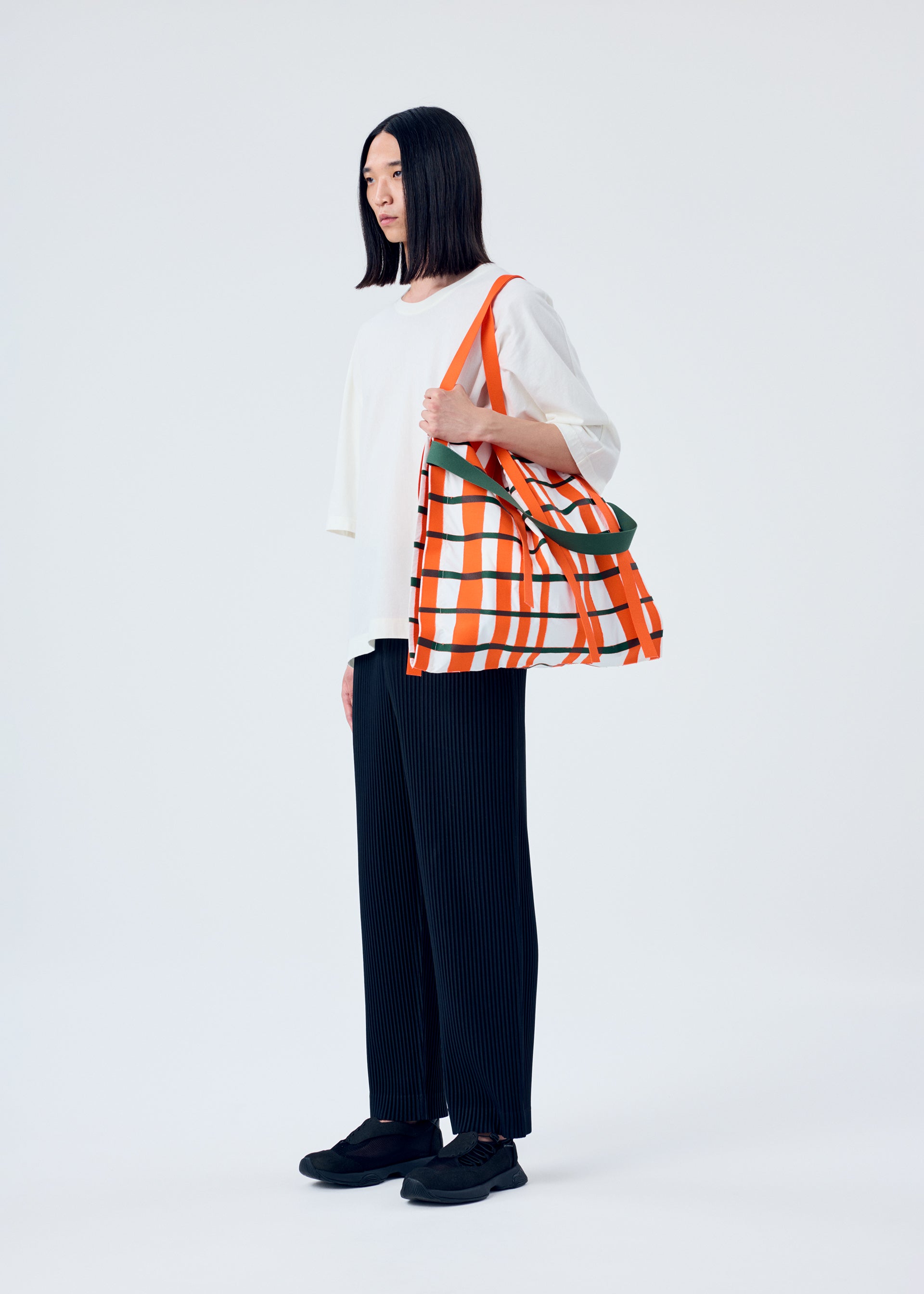A model wears the HOMME PLISSÉ ISSEY MIYAKE WINDSWEPT PLAID BAG bag.