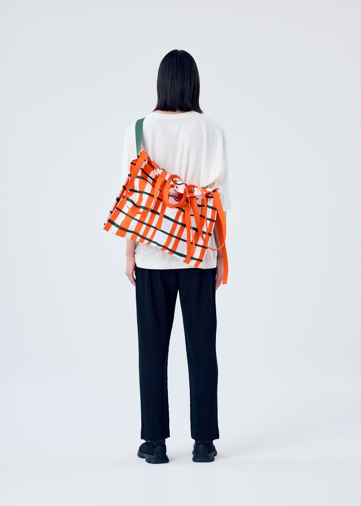 A model wears the HOMME PLISSÉ ISSEY MIYAKE WINDSWEPT PLAID BAG bag.