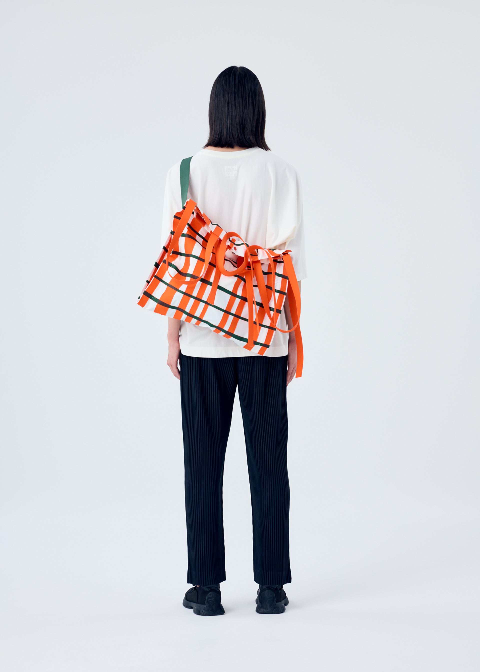 A model wears the HOMME PLISSÉ ISSEY MIYAKE WINDSWEPT PLAID BAG bag.