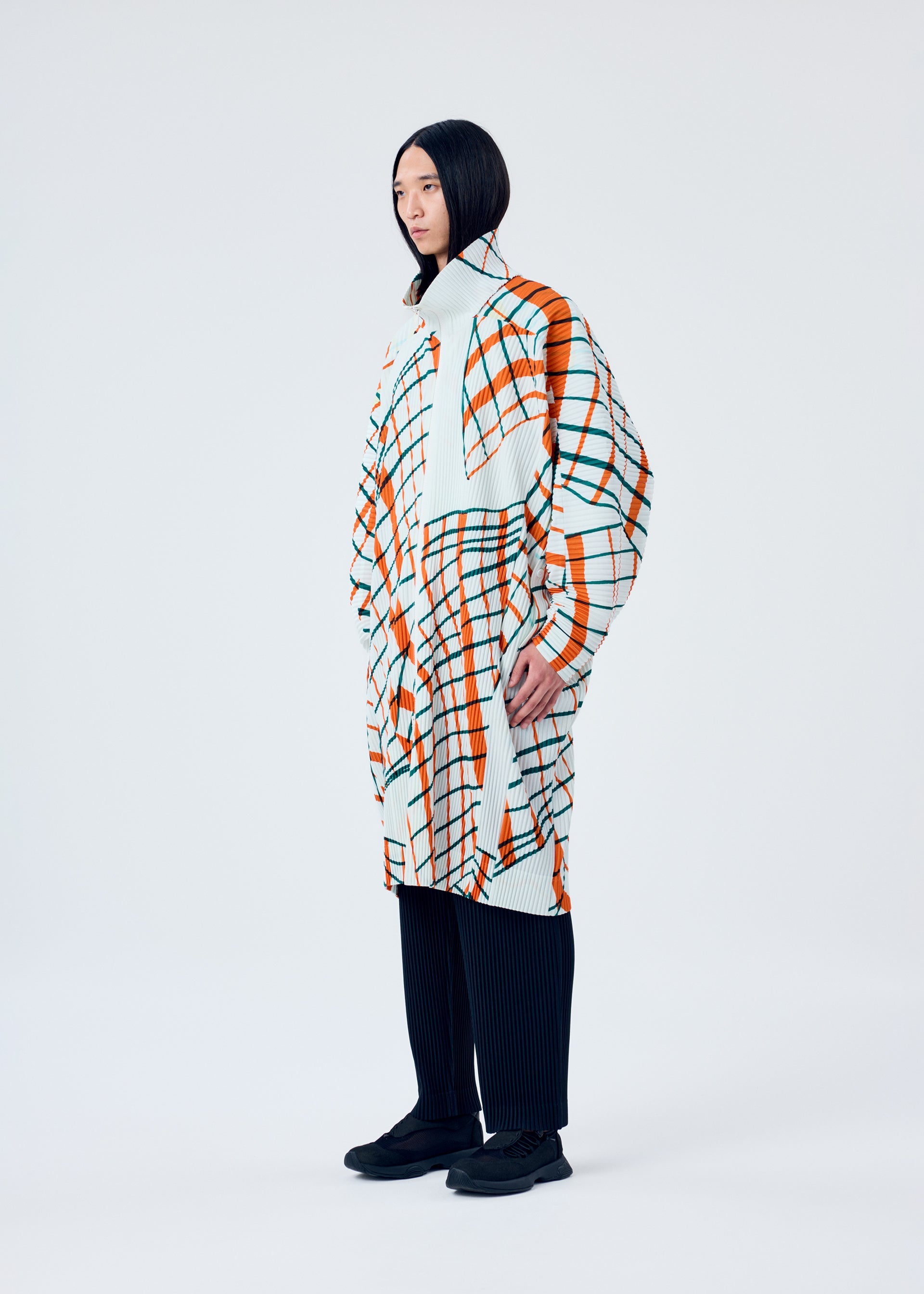 A model wears the HOMME PLISSÉ ISSEY MIYAKE WINDSWEPT PLAID coat.