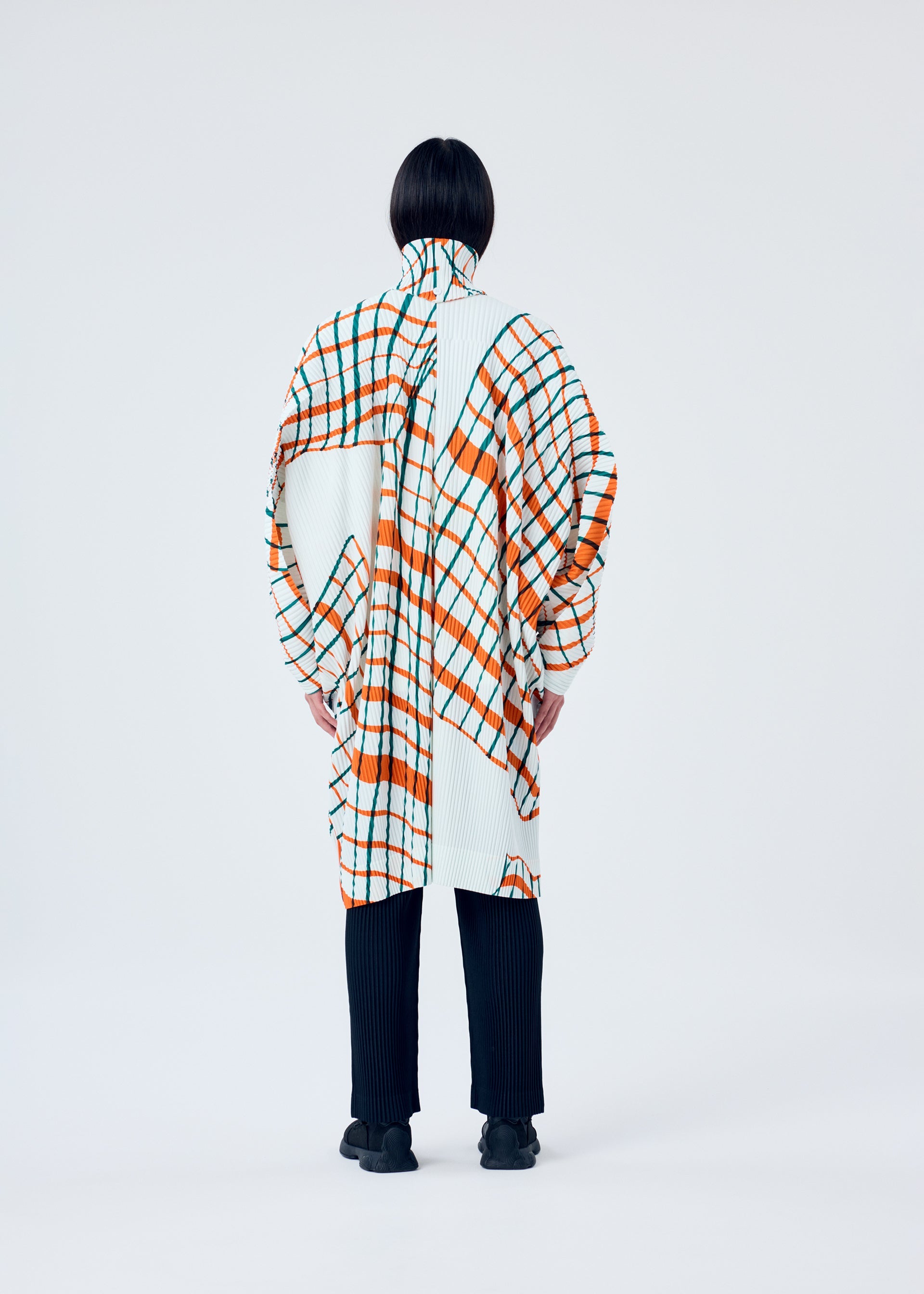 A model wears the HOMME PLISSÉ ISSEY MIYAKE WINDSWEPT PLAID coat.