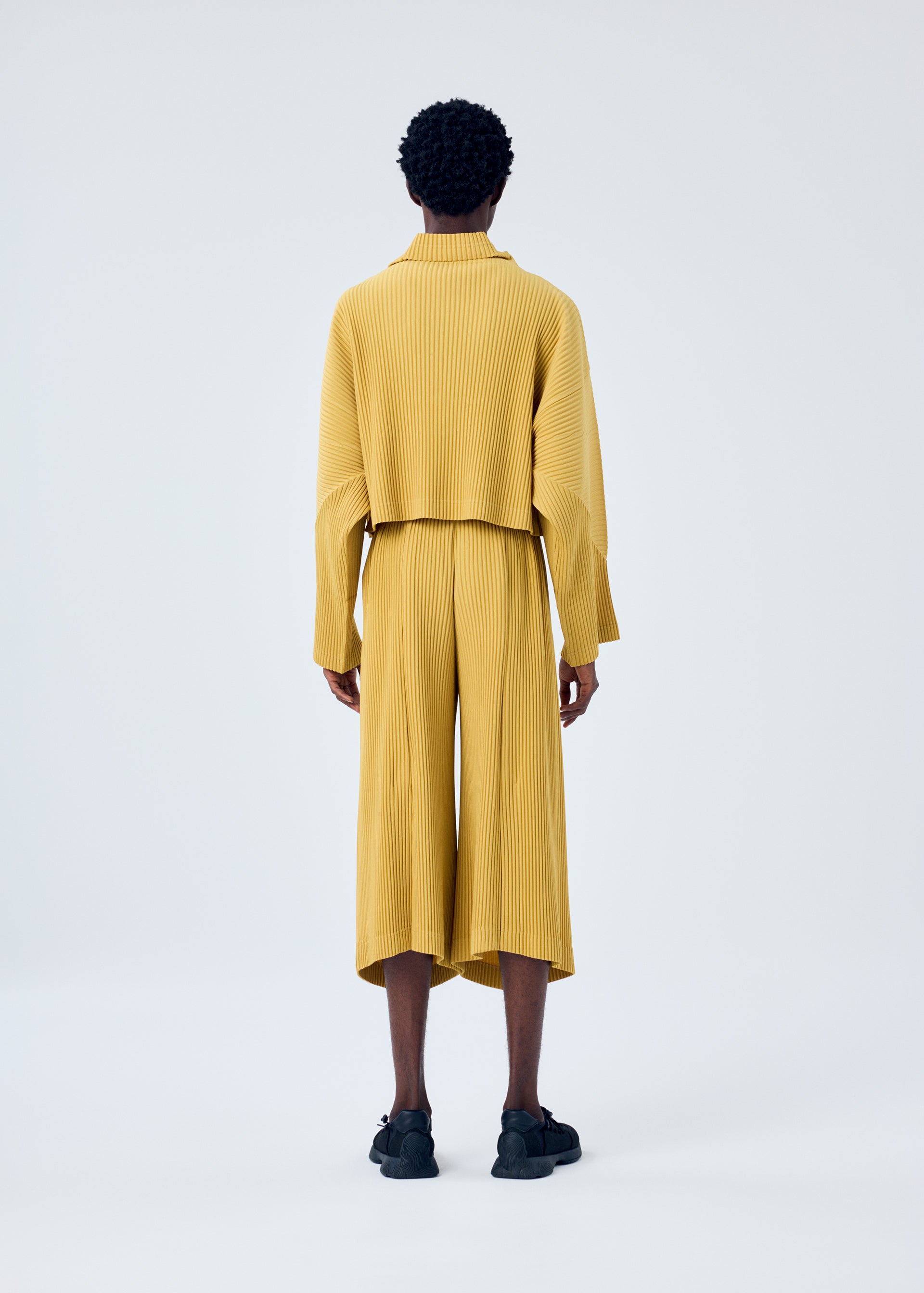 A model wears the HOMME PLISSÉ ISSEY MIYAKE MC JUNE trousers.