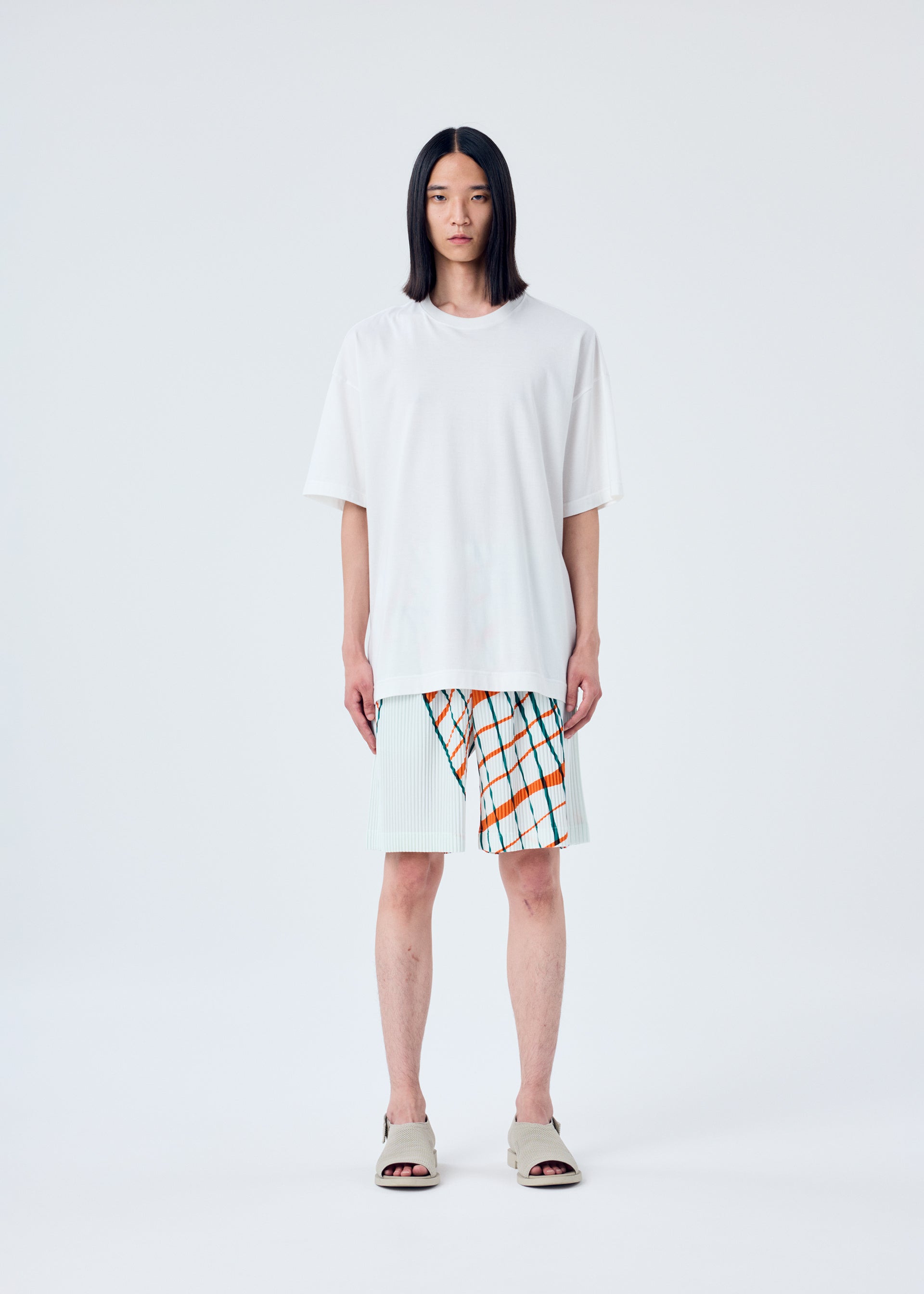 A model wears the HOMME PLISSÉ ISSEY MIYAKE WINDSWEPT PLAID trousers.