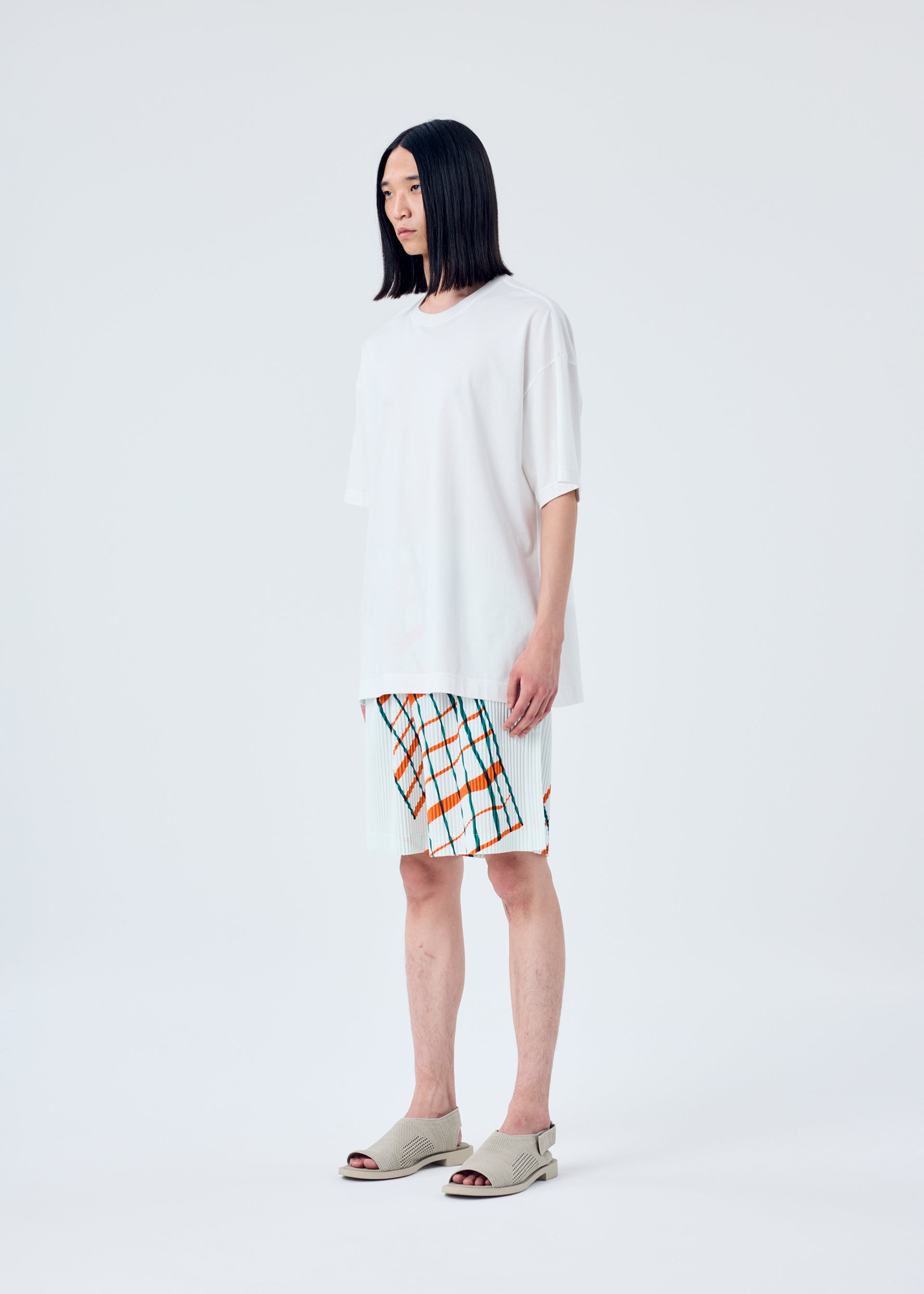 A model wears the HOMME PLISSÉ ISSEY MIYAKE WINDSWEPT PLAID trousers.