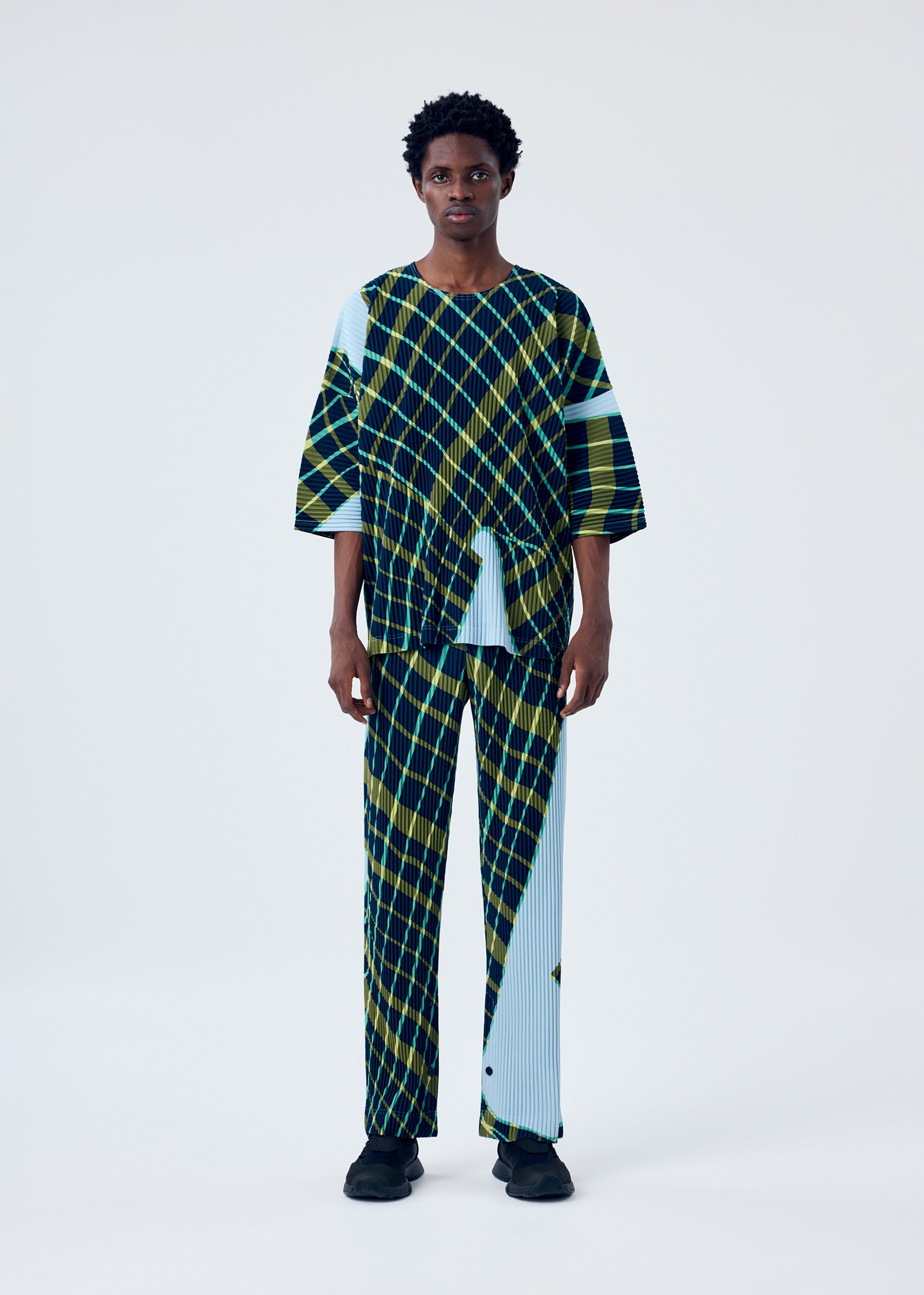 A model wears the HOMME PLISSÉ ISSEY MIYAKE WINDSWEPT PLAID top.