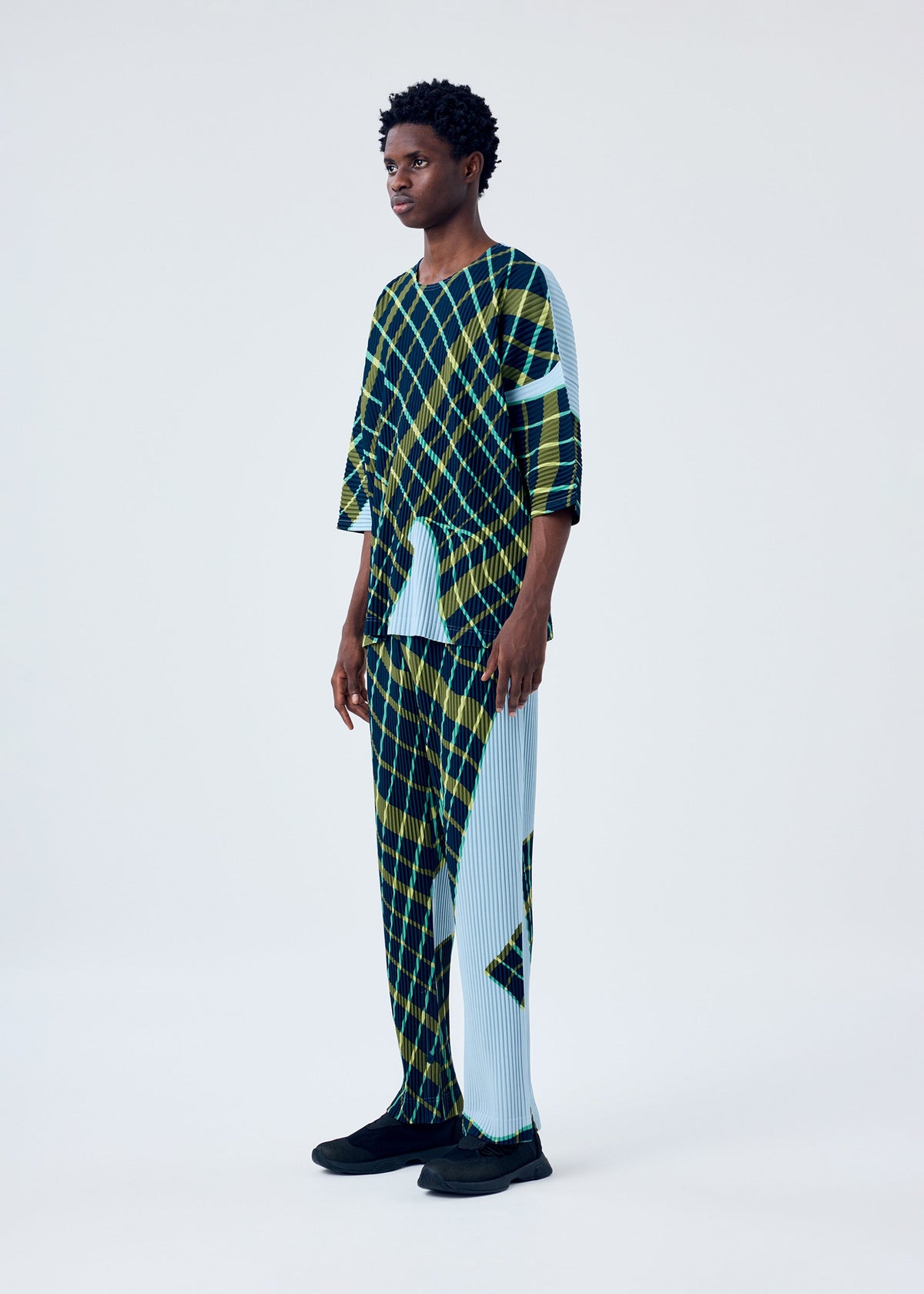 A model wears the HOMME PLISSÉ ISSEY MIYAKE WINDSWEPT PLAID top.