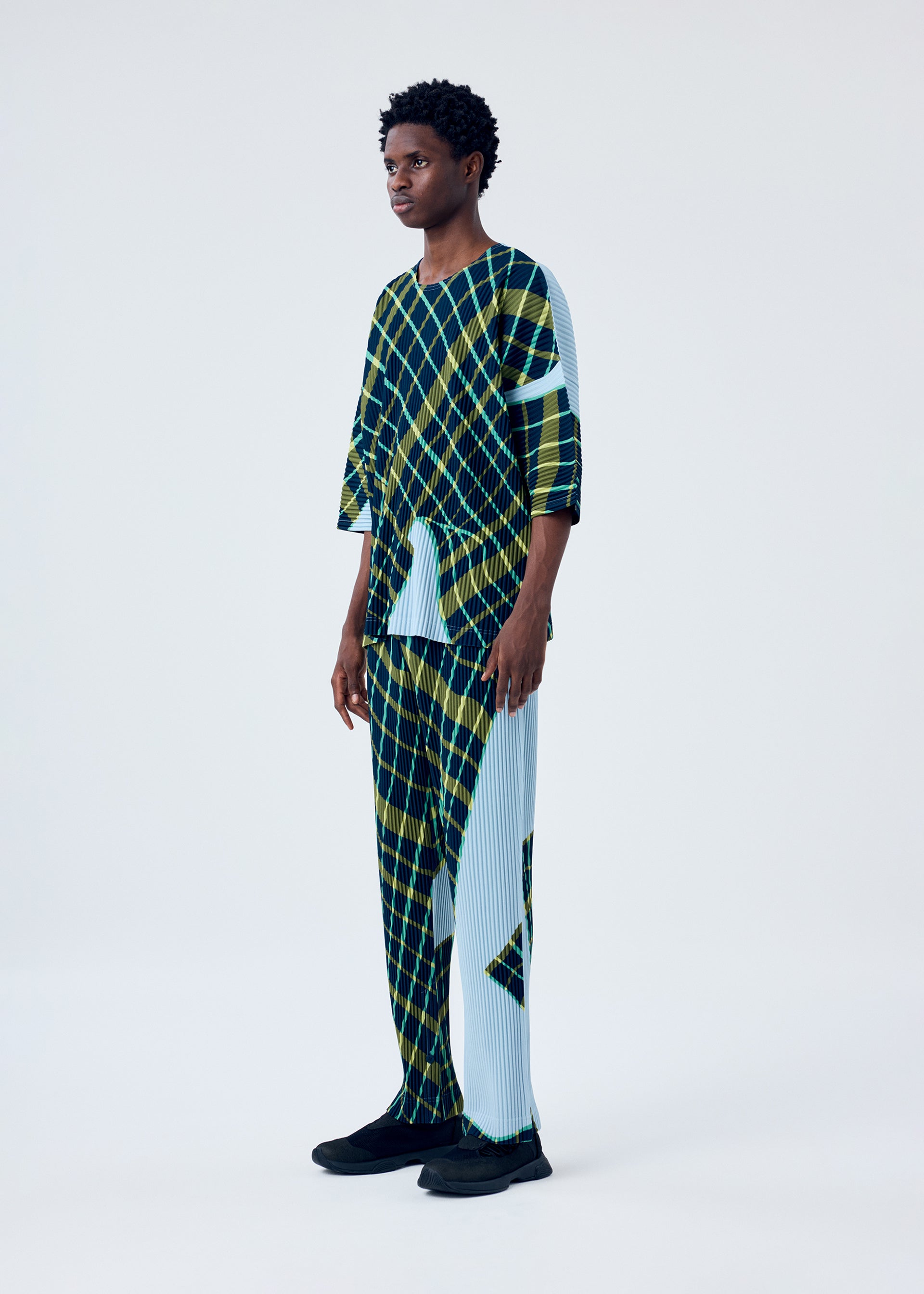 A model wears the HOMME PLISSÉ ISSEY MIYAKE WINDSWEPT PLAID top.