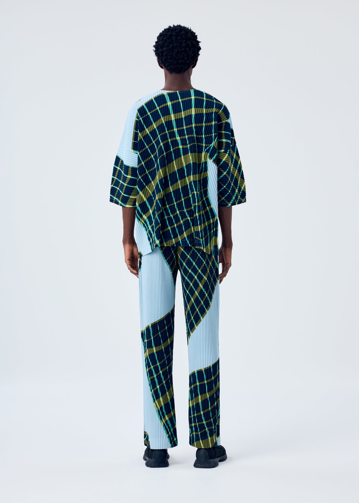A model wears the HOMME PLISSÉ ISSEY MIYAKE WINDSWEPT PLAID top.