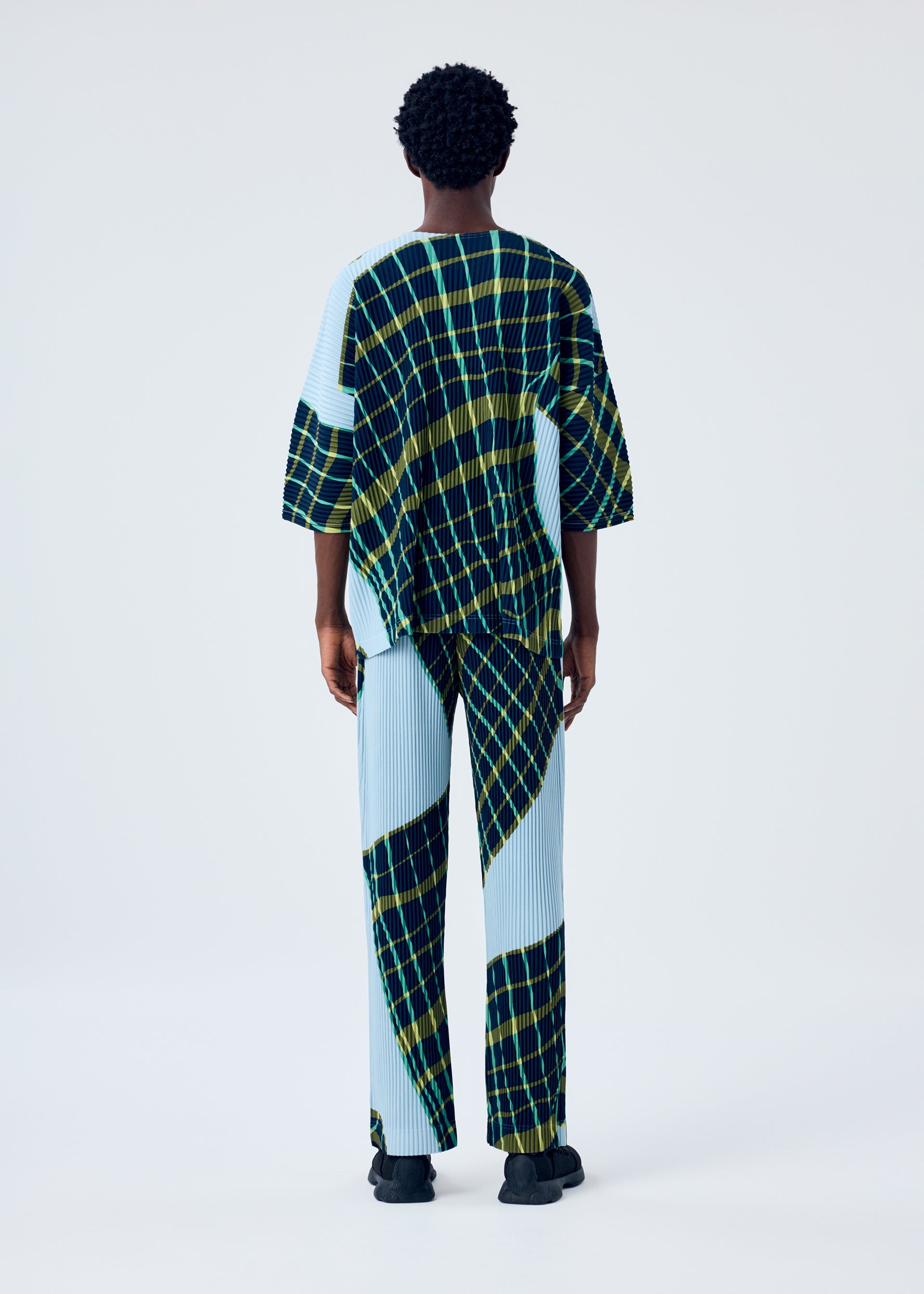 A model wears the HOMME PLISSÉ ISSEY MIYAKE WINDSWEPT PLAID top.
