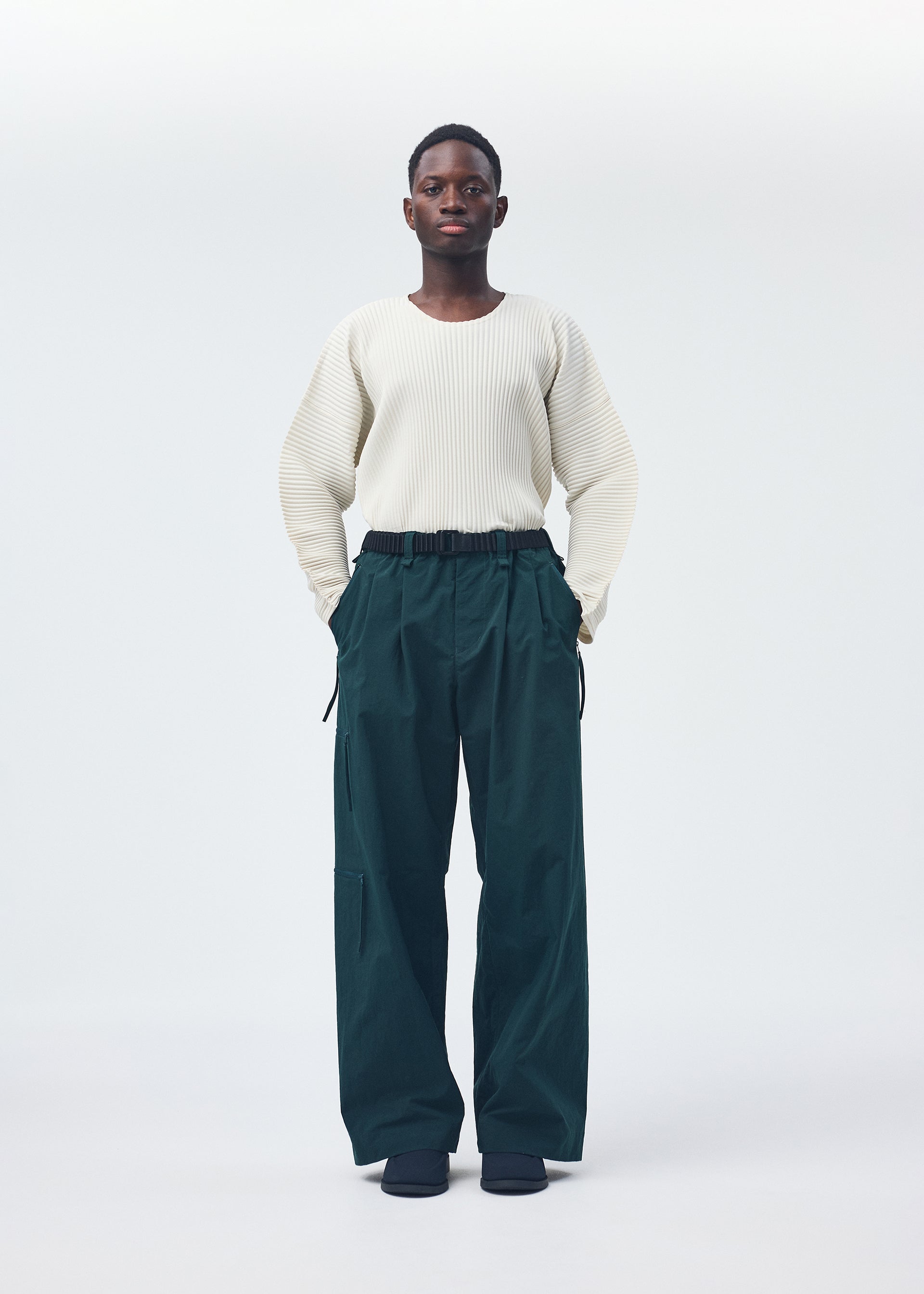 A model wears the HOMME PLISSÉ ISSEY MIYAKE QUARRY PANTS trousers.