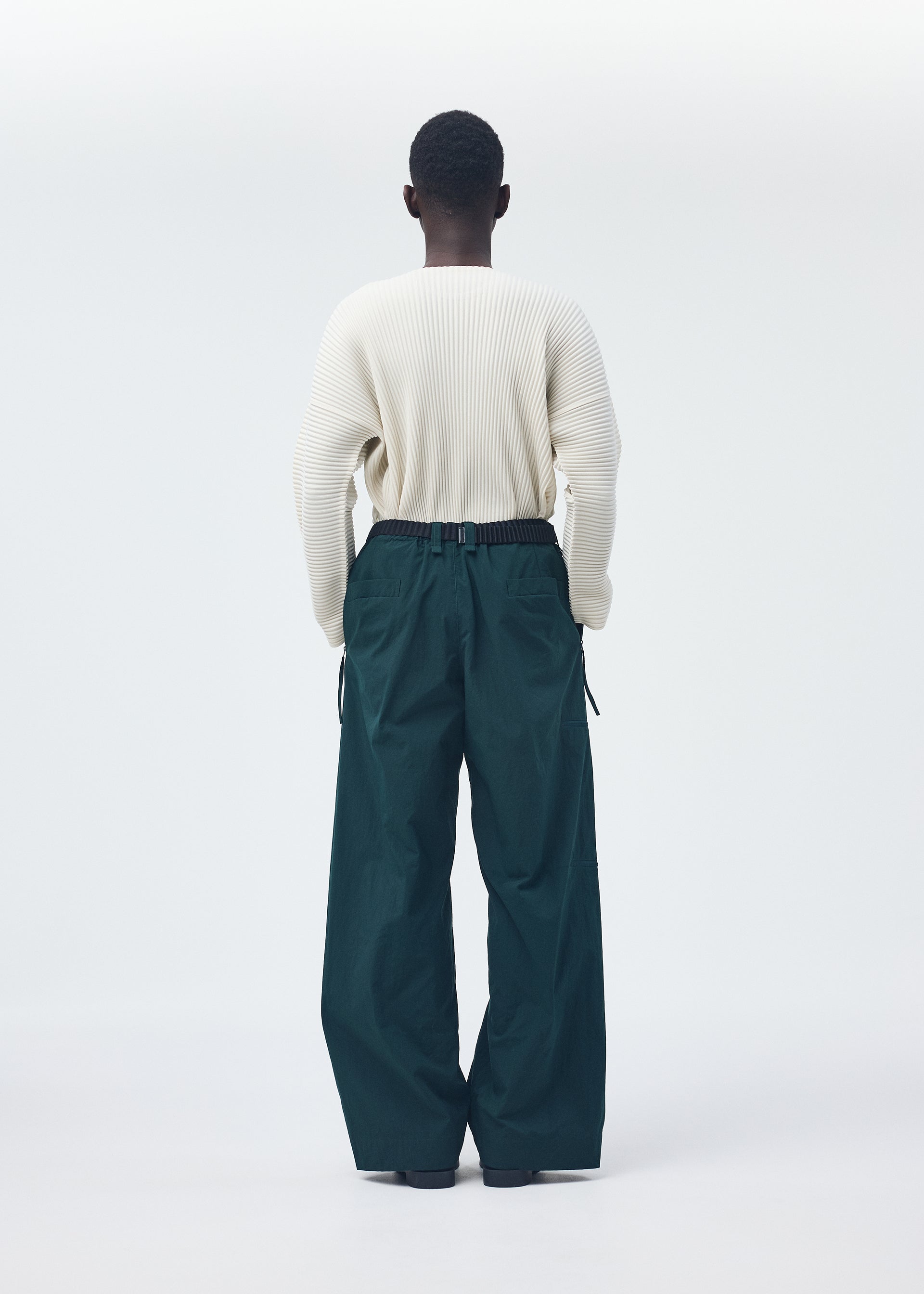 A model wears the HOMME PLISSÉ ISSEY MIYAKE QUARRY PANTS trousers.