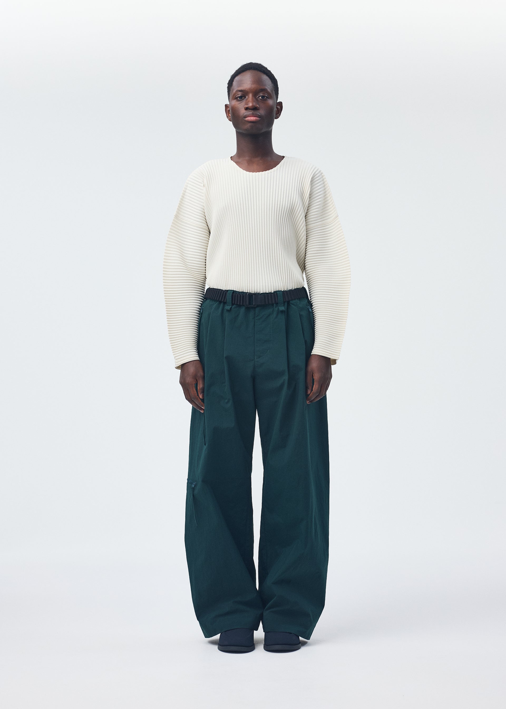 A model wears the HOMME PLISSÉ ISSEY MIYAKE QUARRY PANTS trousers.
