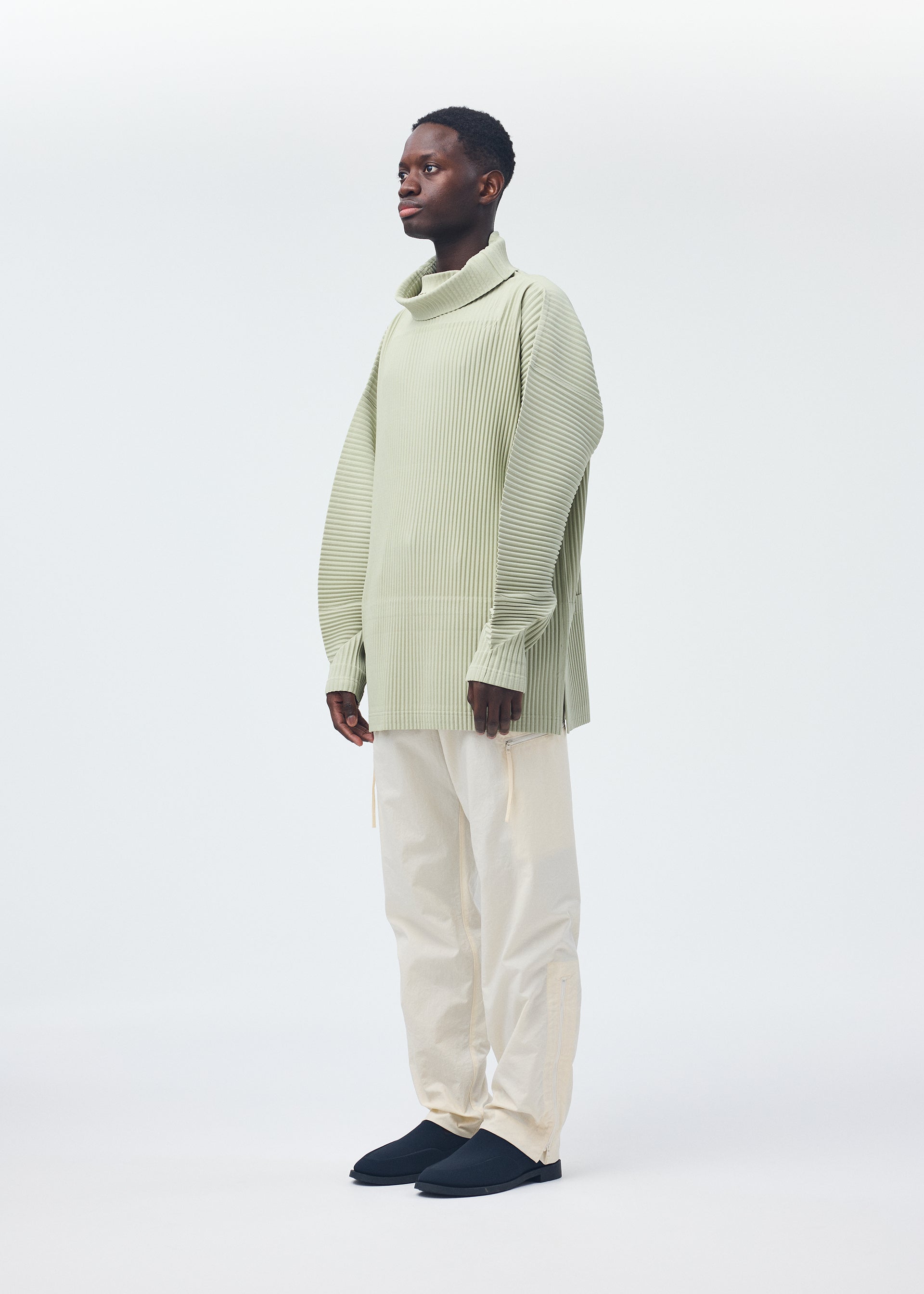 A model wears the HOMME PLISSÉ ISSEY MIYAKE QUARRY PANTS trousers.