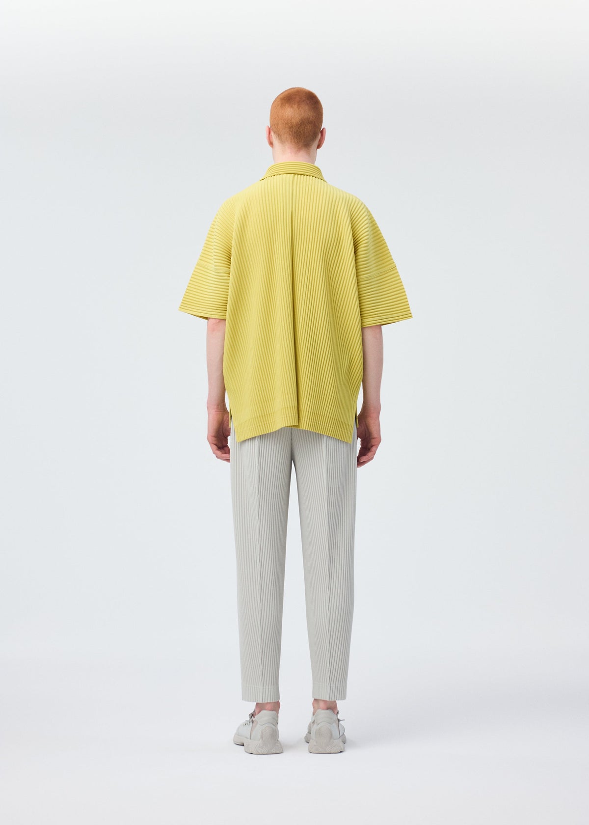 A model wears the HOMME PLISSÉ ISSEY MIYAKE COMPLEAT TROUSERS trousers.