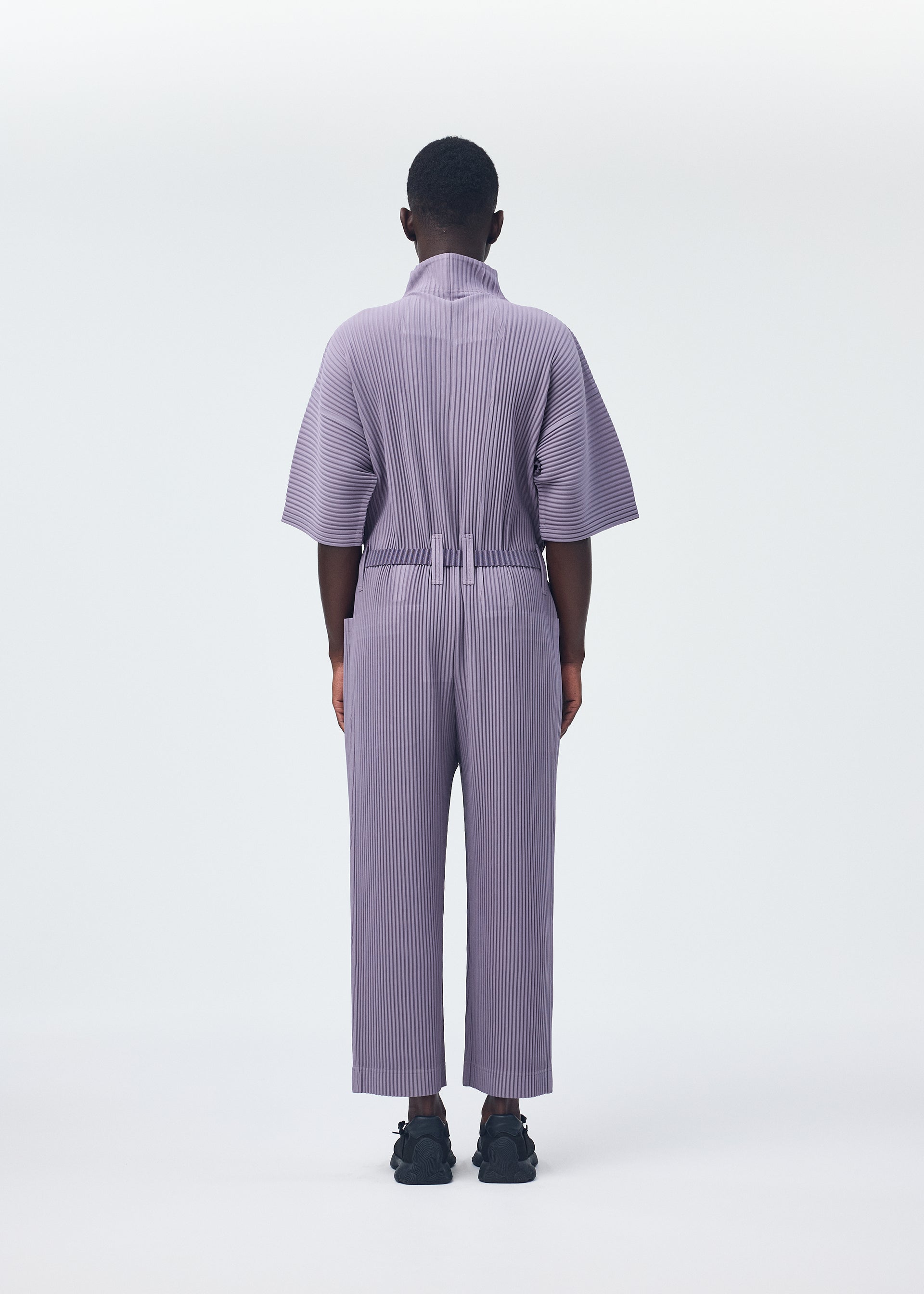 A model wears the HOMME PLISSÉ ISSEY MIYAKE PLEATS BOTTOMS 1 jumpsuit.