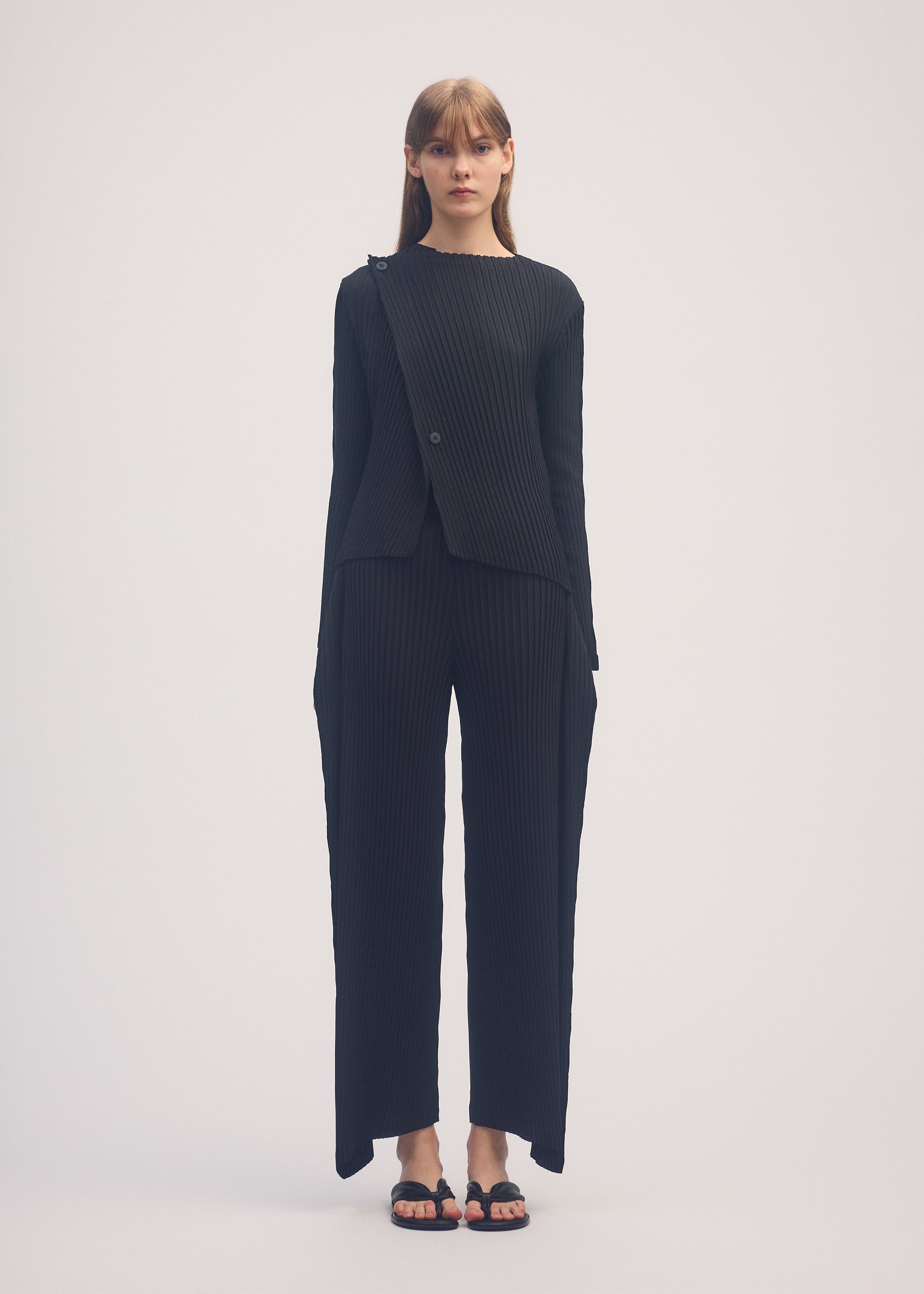 A model wears the ISSEY MIYAKE SHADOW STUDY PLEATS SOLID trousers.