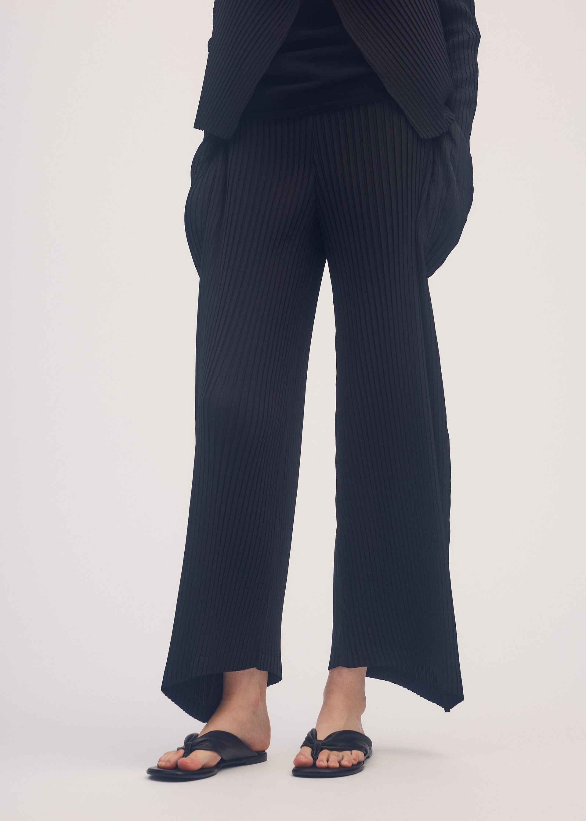 A model wears the ISSEY MIYAKE SHADOW STUDY PLEATS SOLID trousers.