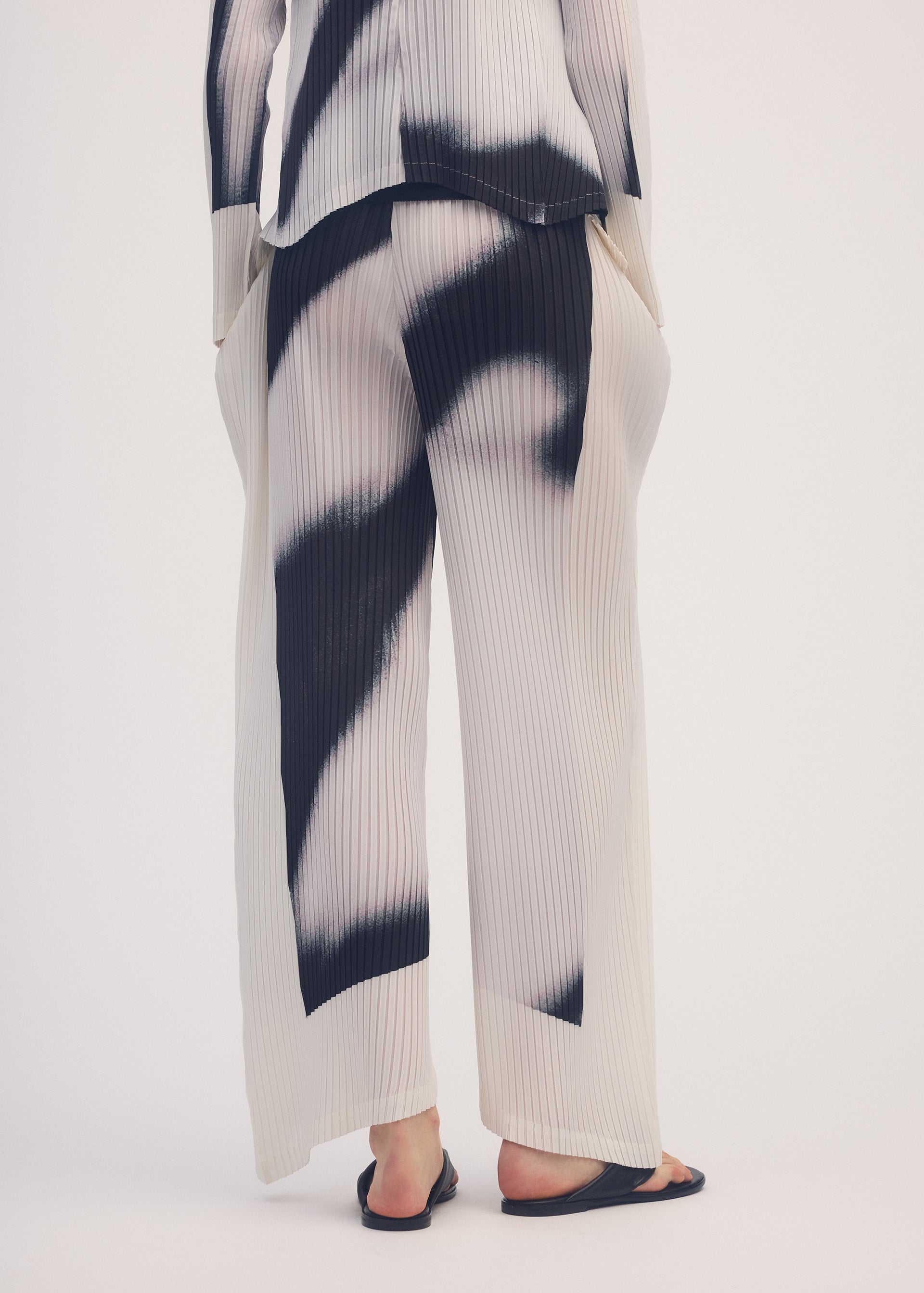A model wears the ISSEY MIYAKE SHADOW STUDY PLEATS trousers.
