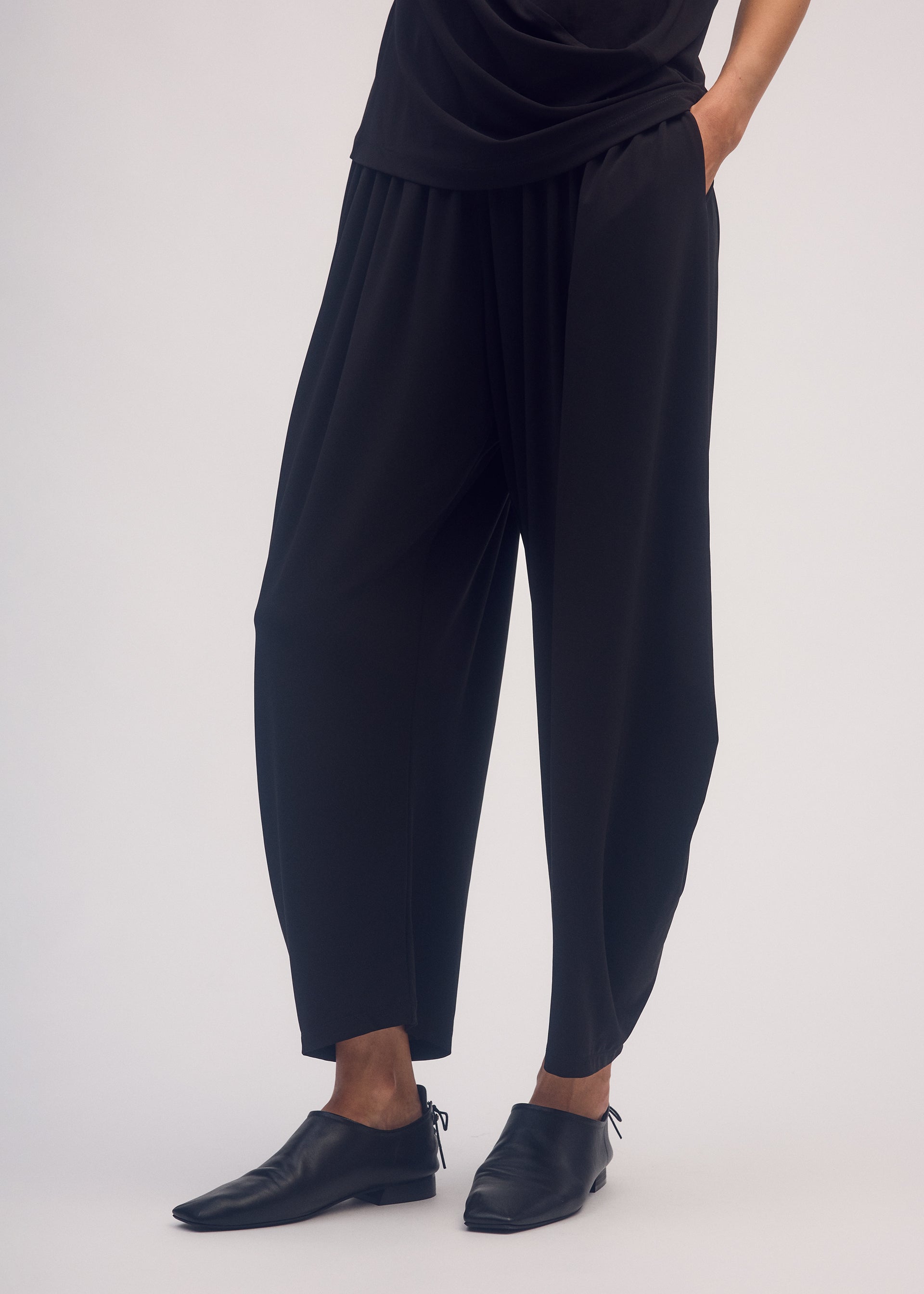 A model wears the ISSEY MIYAKE DRAPE JERSEY 56 trousers.