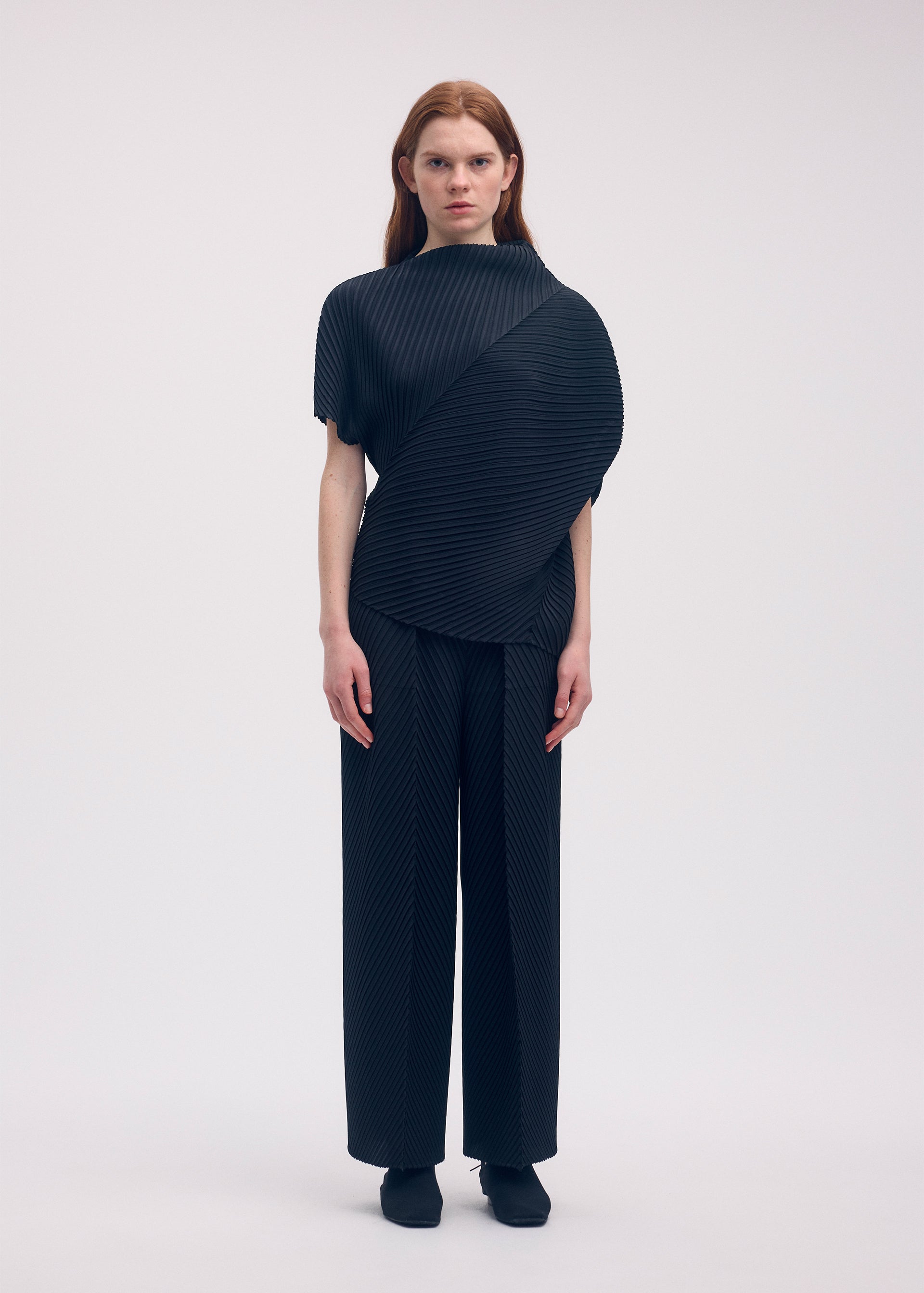 A model wears the ISSEY MIYAKE SOFT FOLD PLEATS trousers.