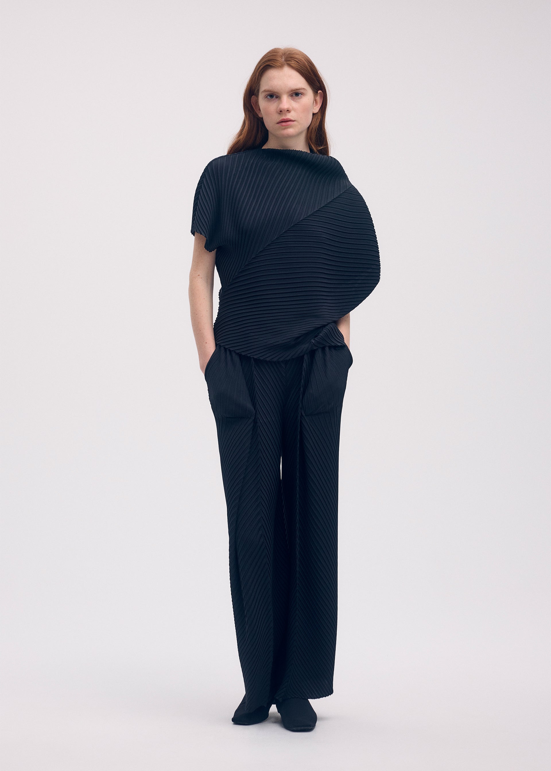 A model wears the ISSEY MIYAKE SOFT FOLD PLEATS trousers.