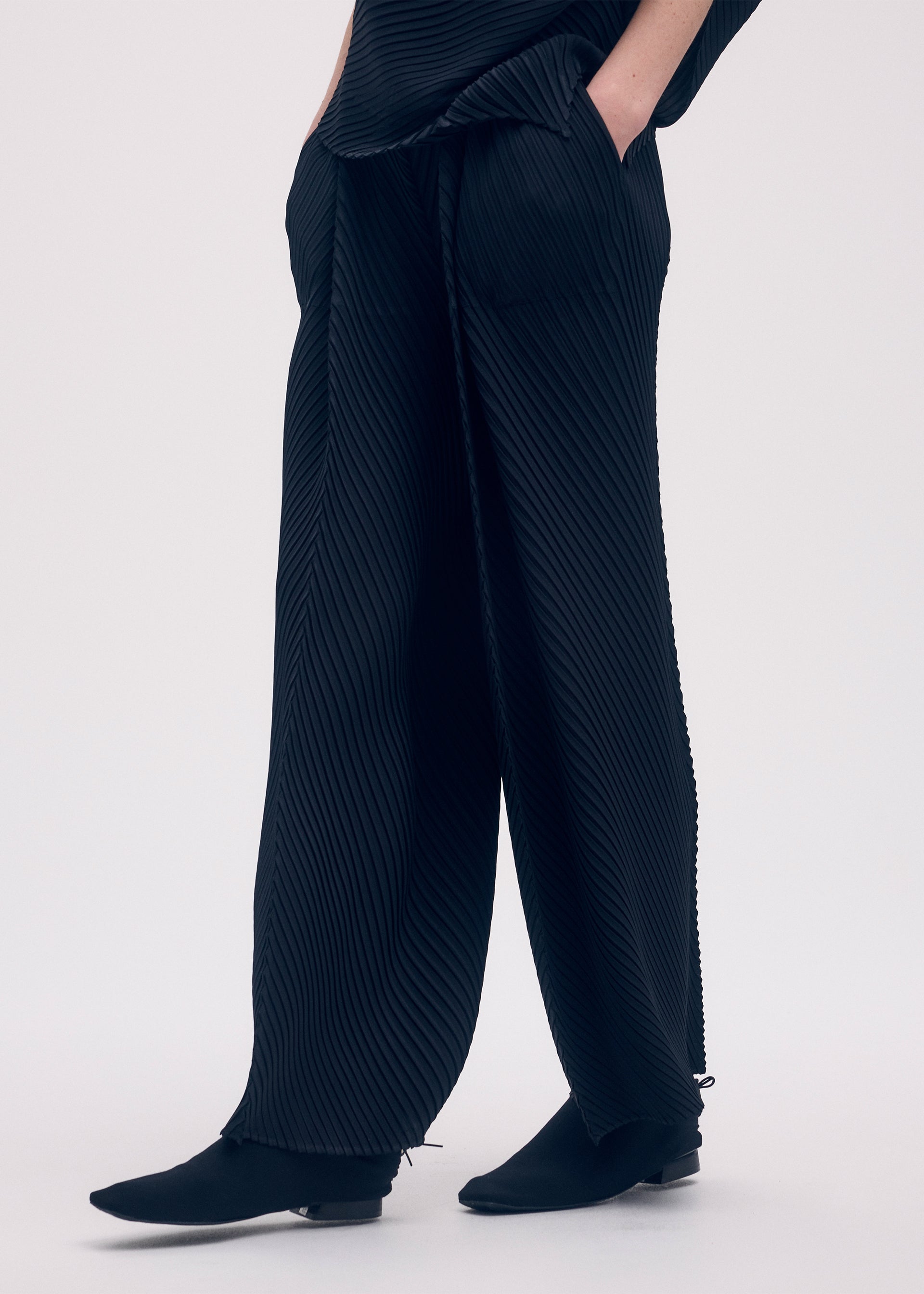 A model wears the ISSEY MIYAKE SOFT FOLD PLEATS trousers.