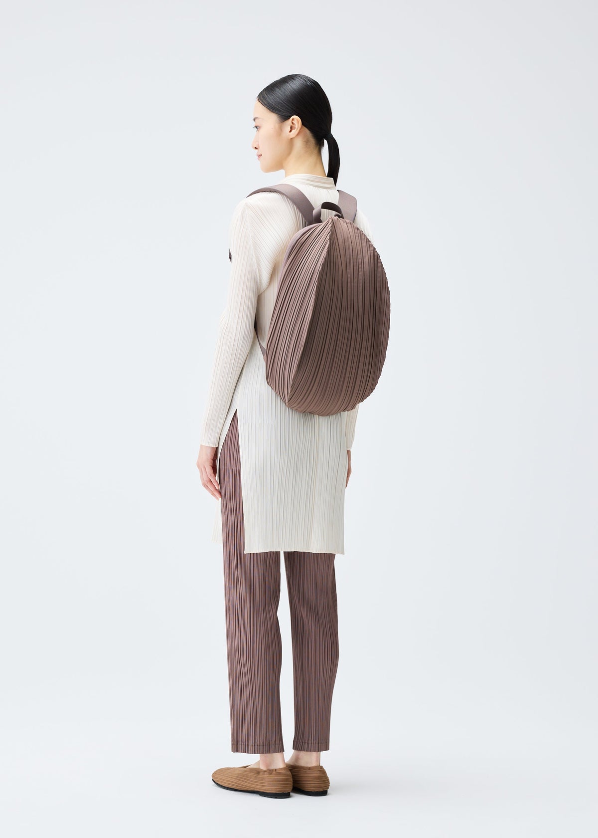 A model wears the PLEATS PLEASE ISSEY MIYAKE OVAL PLEATS BACKPACK bag.