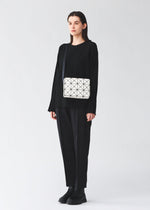 A model wears the BAO BAO ISSEY MIYAKE CUBOID cuboid-shoulder-bag-adjustable-strap-larger-size-off-white.