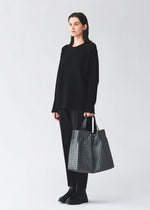 A model wears the BAO BAO ISSEY MIYAKE CART REFLECTOR cart-reflector-tote-copper-brown.