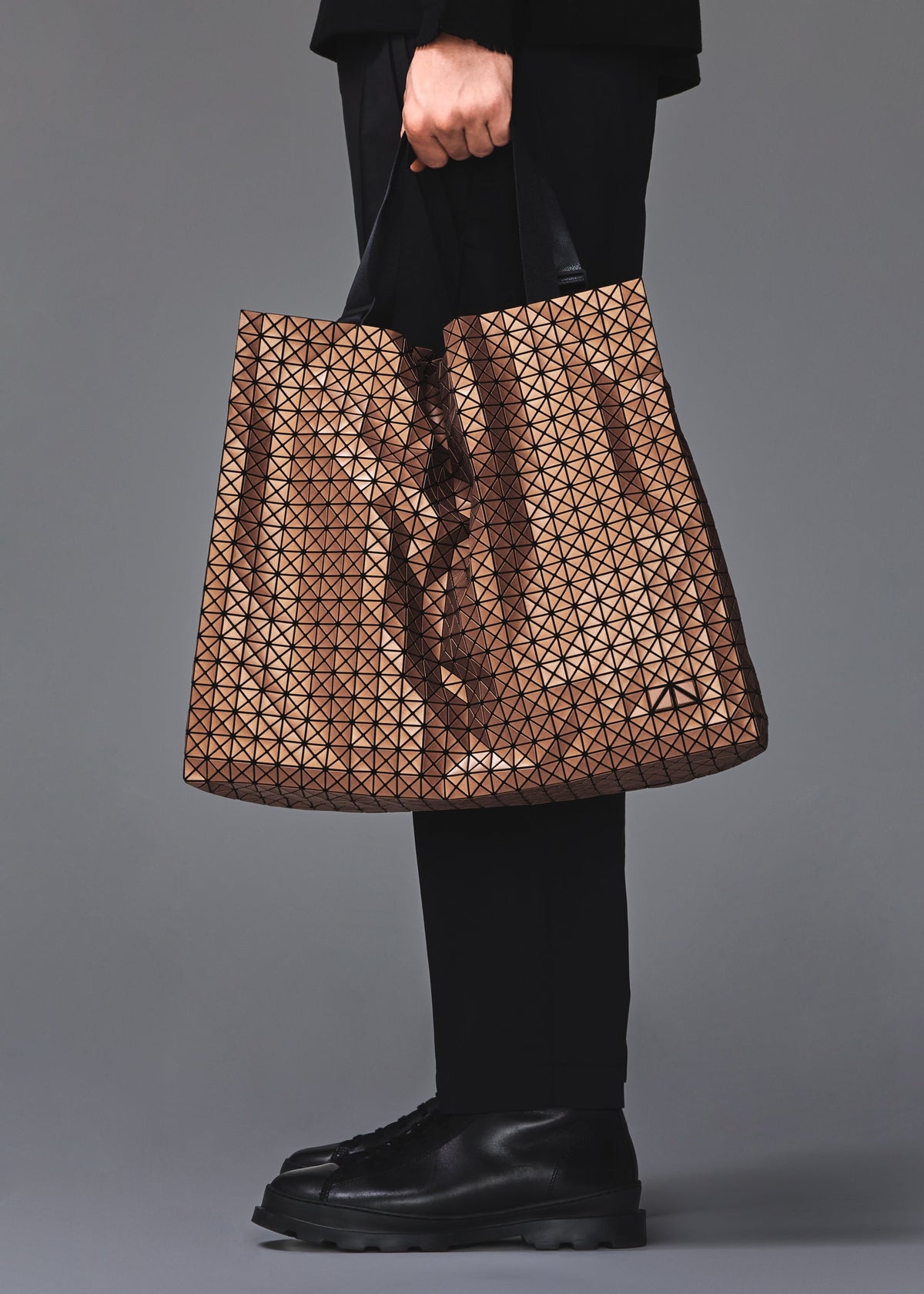 A model wears the BAO BAO ISSEY MIYAKE CART REFLECTOR cart-reflector-tote-copper-brown.