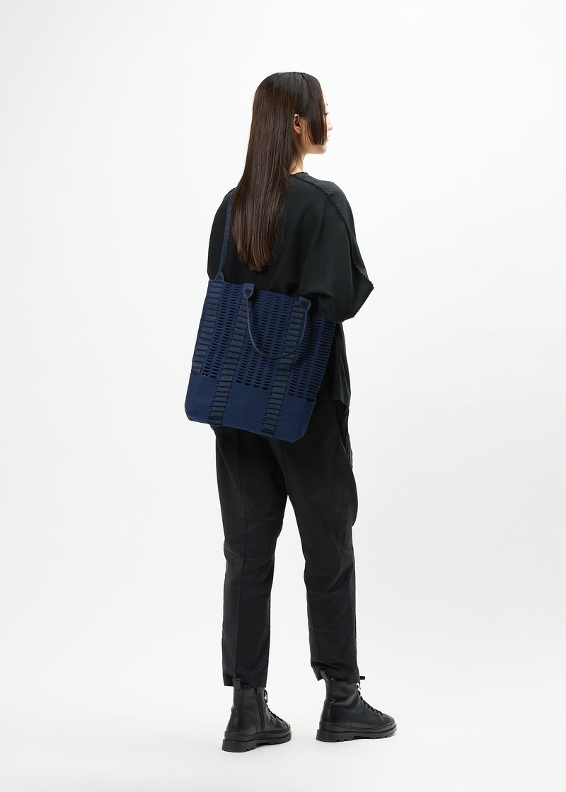 A model wears the GOOD GOODS ISSEY MIYAKE MOKKO MONO bag.