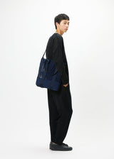 A model wears the GOOD GOODS ISSEY MIYAKE MOKKO MONO bag.