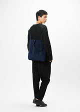 A model wears the GOOD GOODS ISSEY MIYAKE MOKKO MONO bag.