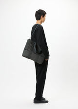 A model wears the GOOD GOODS ISSEY MIYAKE MOKKO MONO bag.