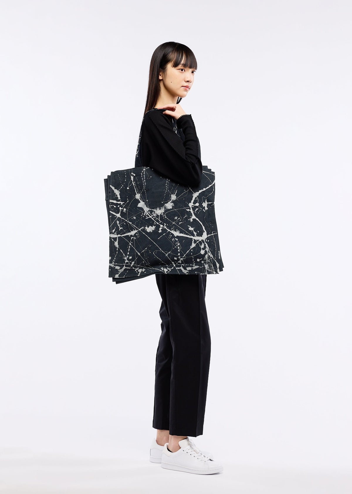 A model wears the GOOD GOODS ISSEY MIYAKE IROGAMI BASSEN bag.