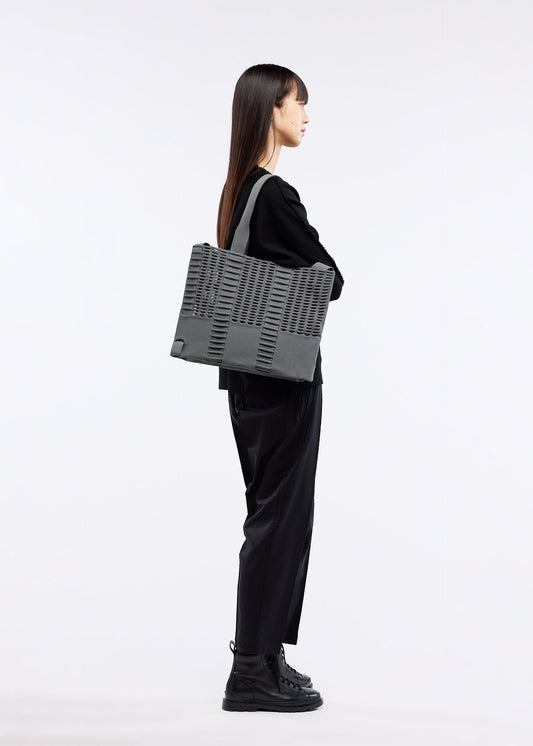 A model wears the GOOD GOODS ISSEY MIYAKE MOKKO MONO bag.