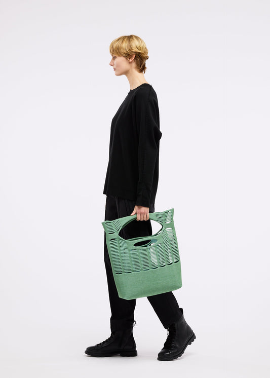 A model wears the GOOD GOODS ISSEY MIYAKE MOKKO TWILL bag.