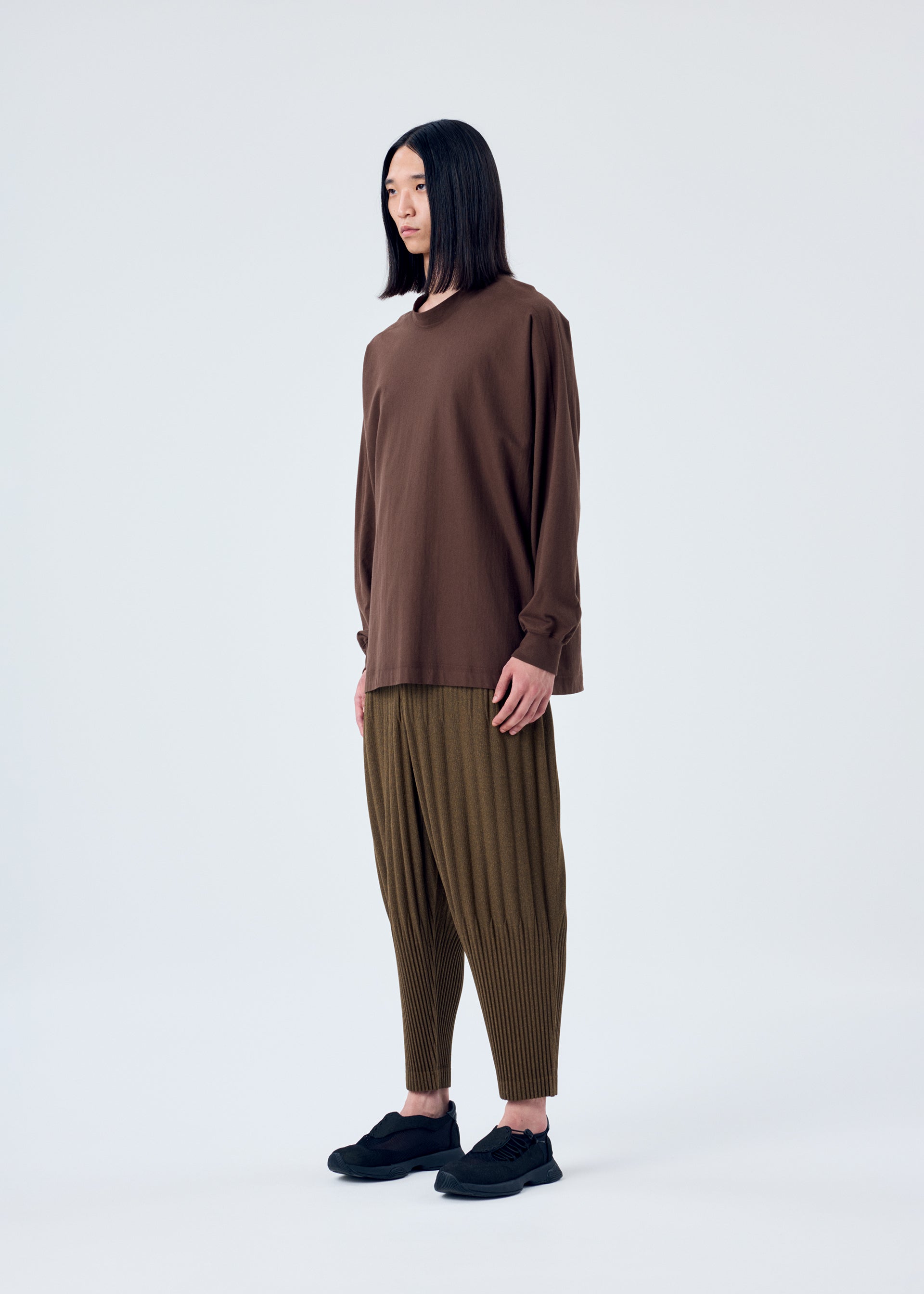 A model wears the HOMME PLISSÉ ISSEY MIYAKE HEATHER PLEATS trousers.