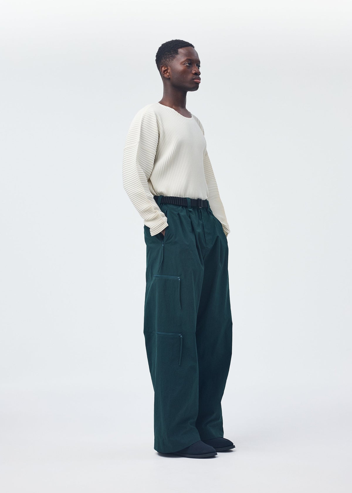 A model wears the HOMME PLISSÉ ISSEY MIYAKE QUARRY PANTS trousers.