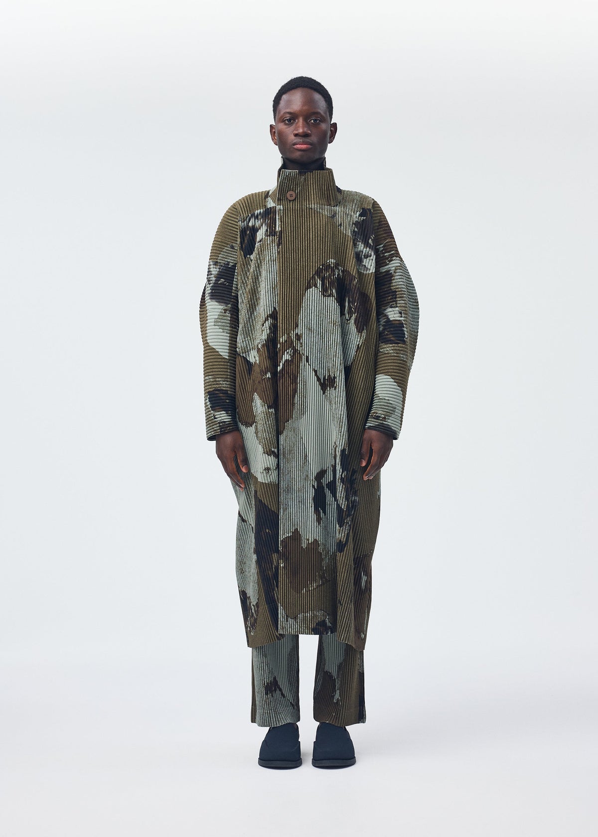 A model wears the HOMME PLISSÉ ISSEY MIYAKE PAINTED STONE clothing.