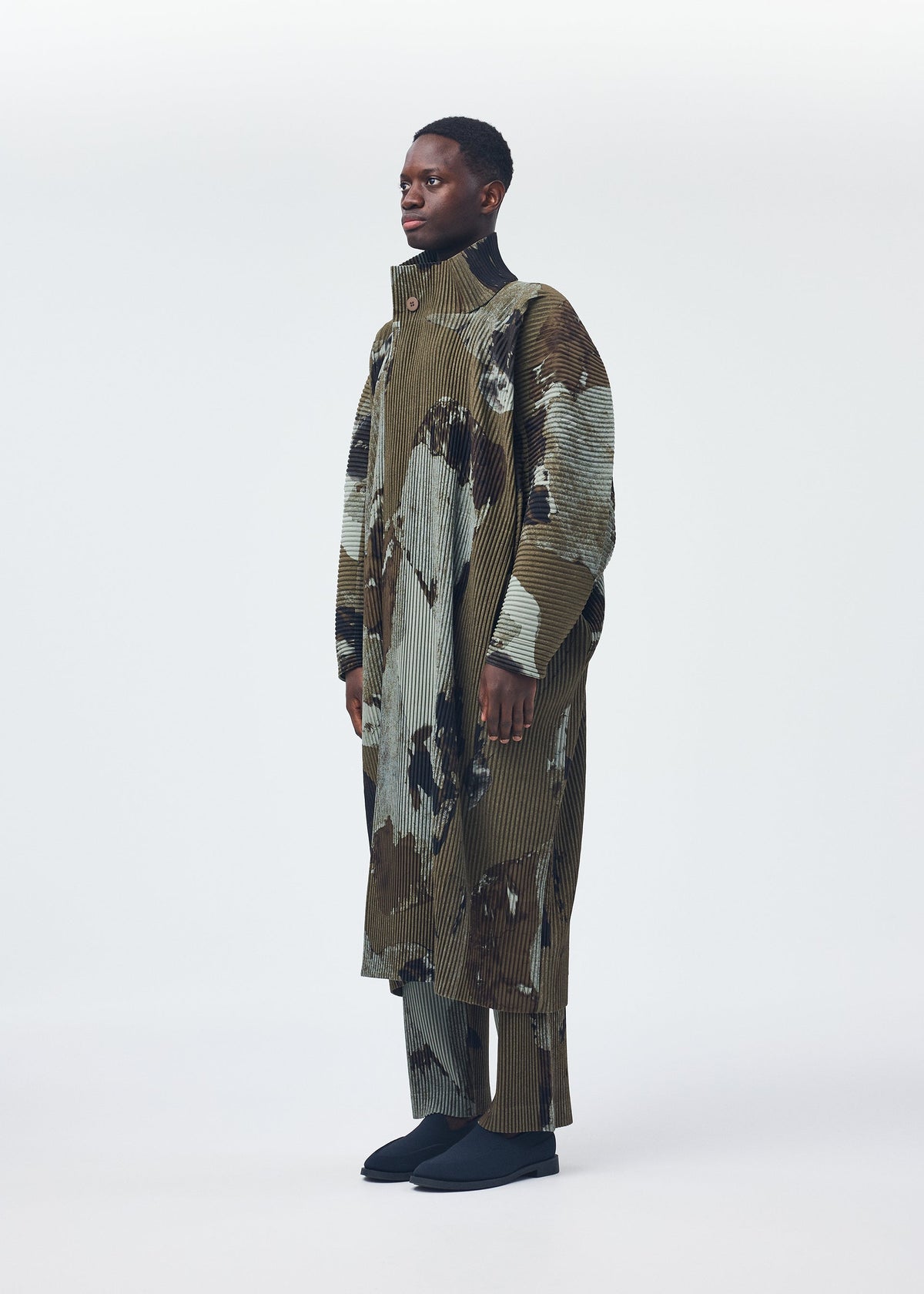 A model wears the HOMME PLISSÉ ISSEY MIYAKE PAINTED STONE clothing.