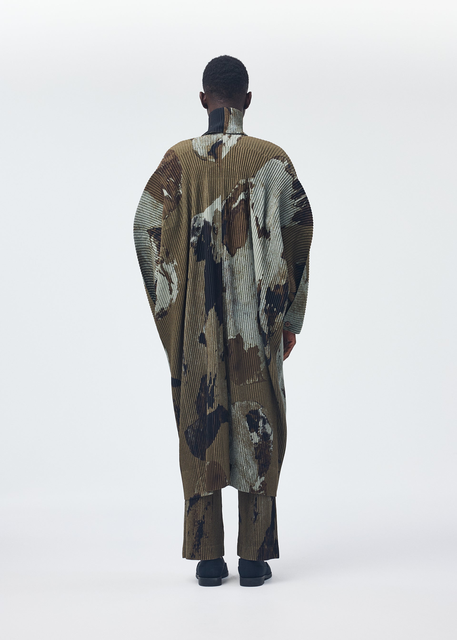 A model wears the HOMME PLISSÉ ISSEY MIYAKE PAINTED STONE clothing.