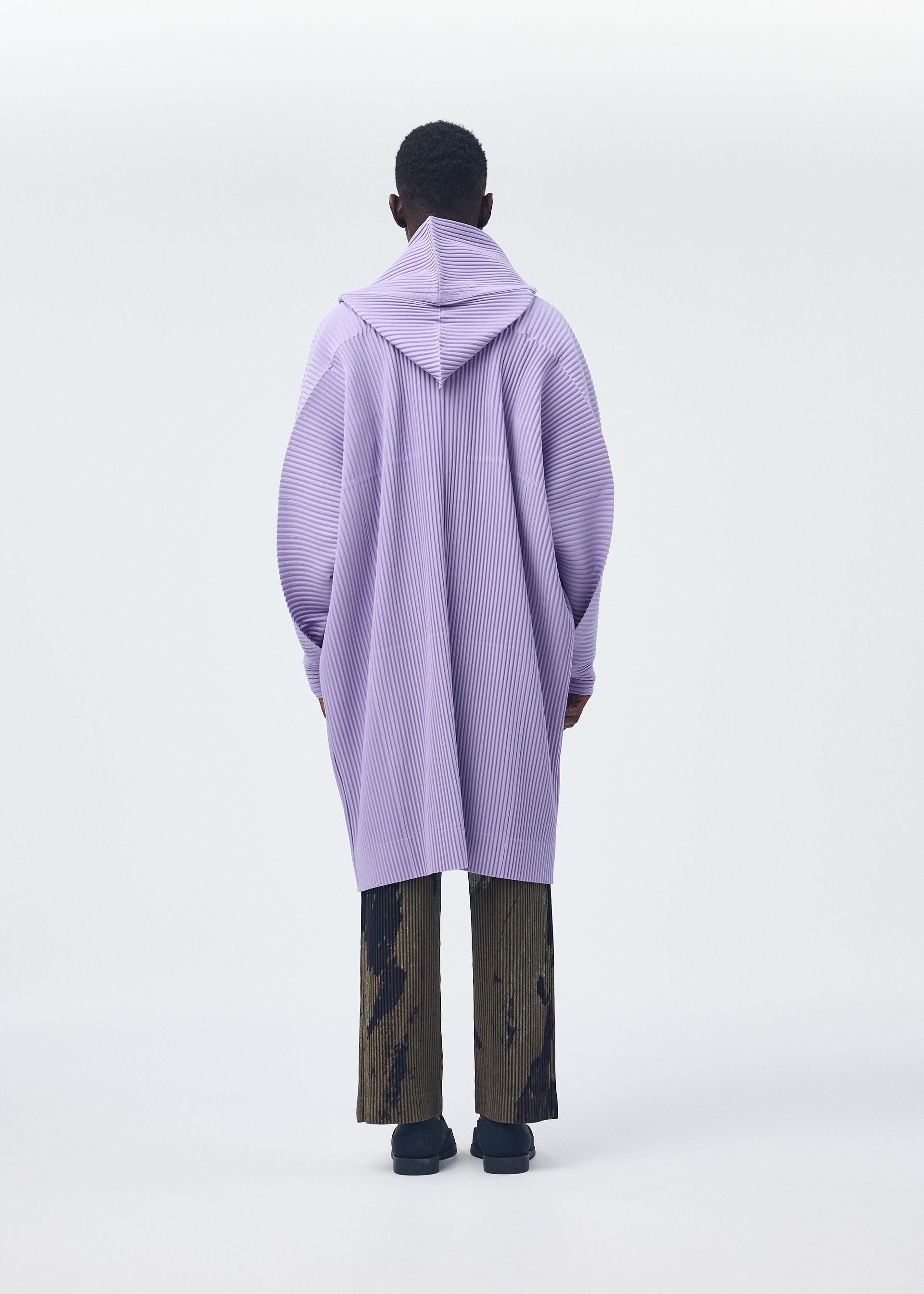 A model wears the HOMME PLISSÉ ISSEY MIYAKE PAINTED STONE clothing.