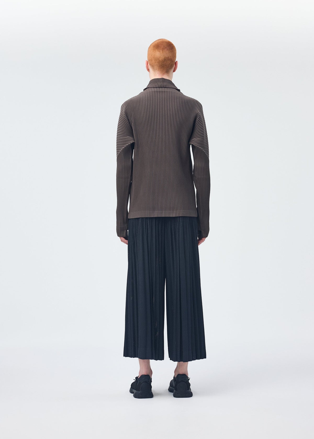 A model wears the HOMME PLISSÉ ISSEY MIYAKE WICKERWORK MESH trousers.