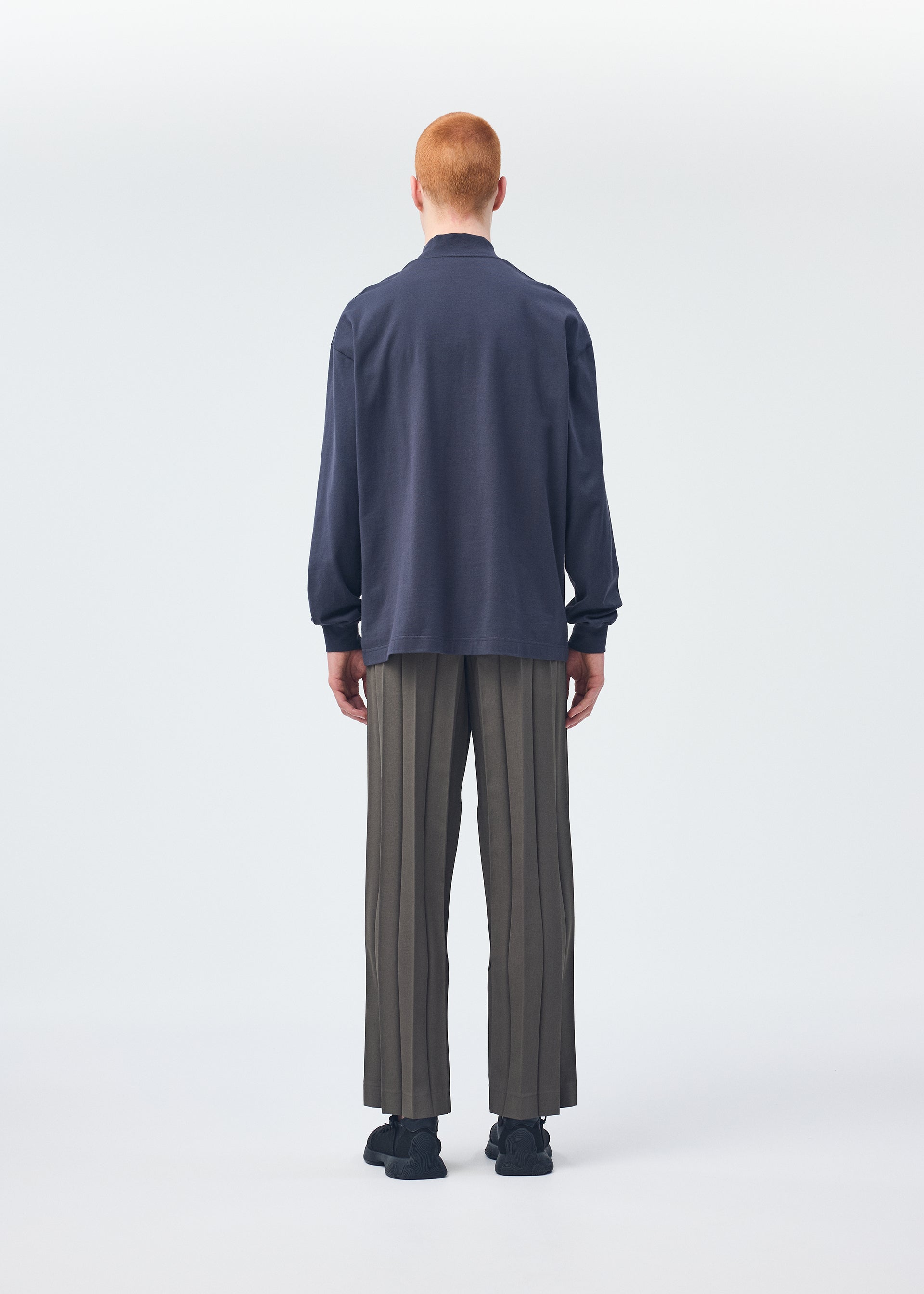 A model wears the HOMME PLISSÉ ISSEY MIYAKE Black Turtleneck Top top.