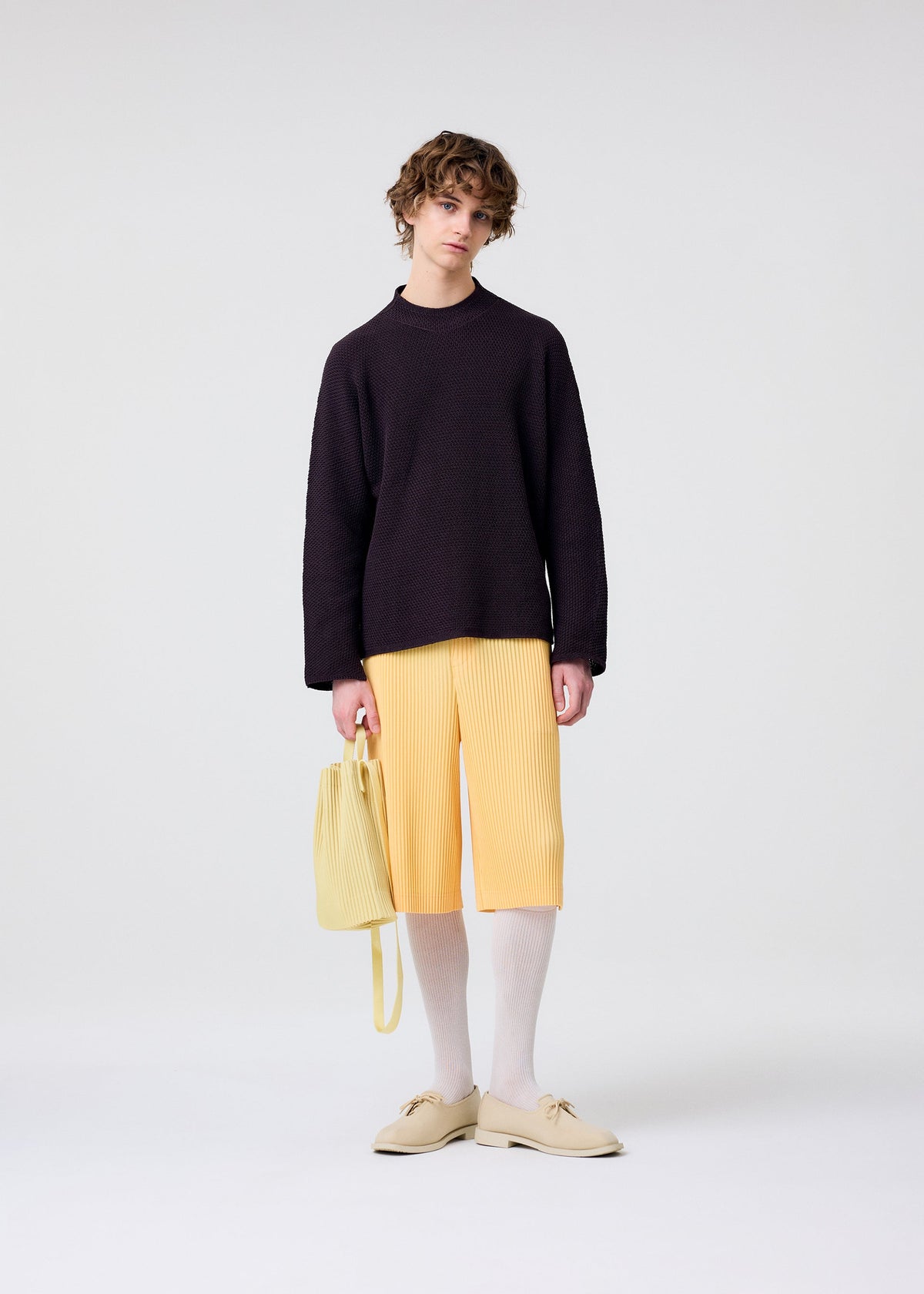 A model wears the HOMME PLISSÉ ISSEY MIYAKE DRAWSTRING PLEATS BAG bag.