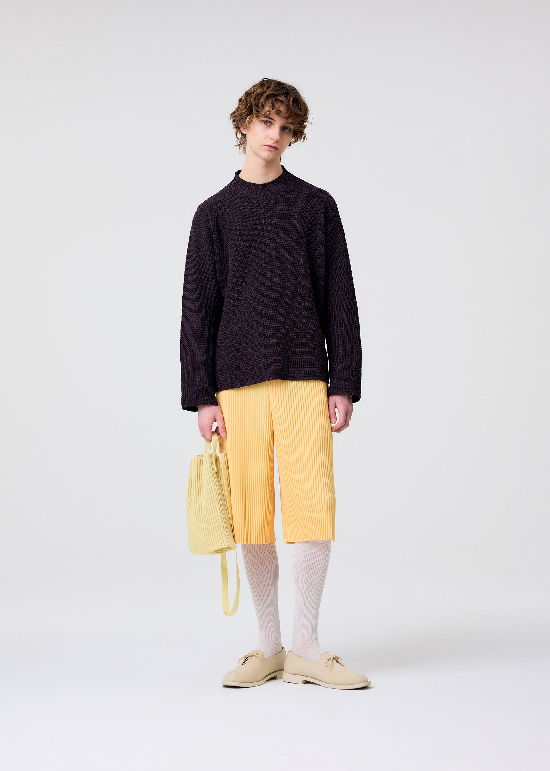 A model wears the HOMME PLISSÉ ISSEY MIYAKE DRAWSTRING PLEATS BAG bag.