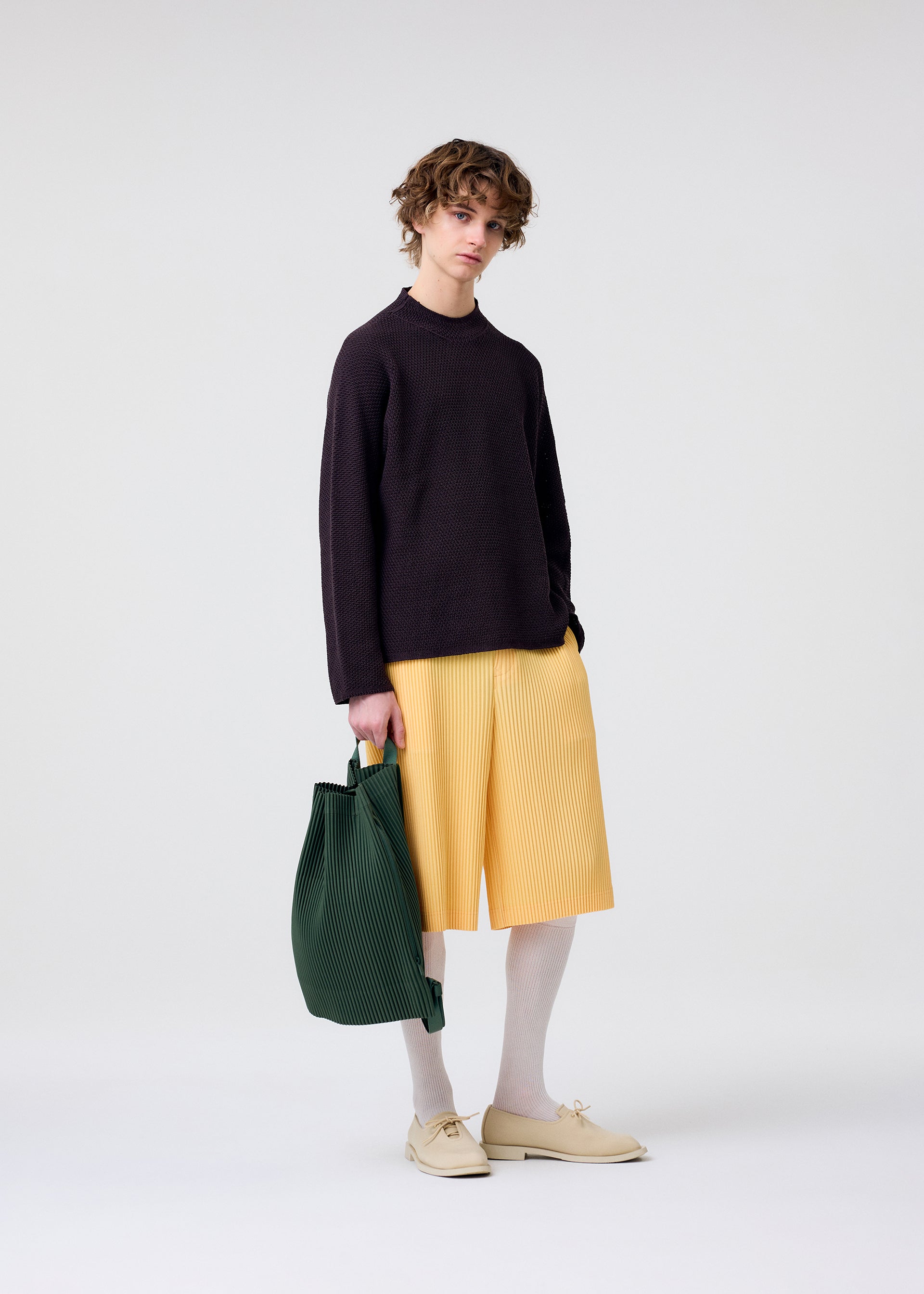 A model wears the HOMME PLISSÉ ISSEY MIYAKE DRAWSTRING PLEATS BAG bag.
