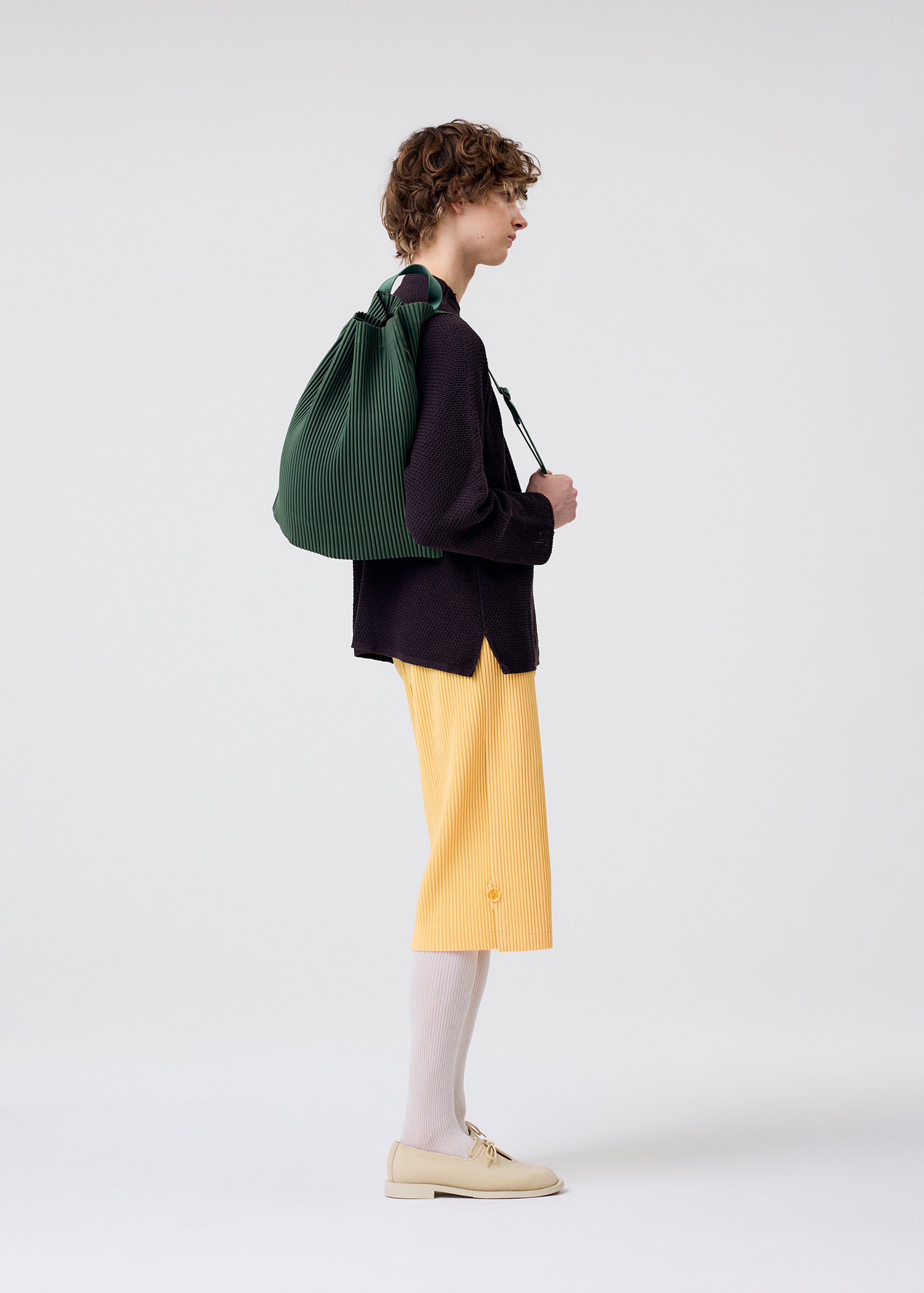 A model wears the HOMME PLISSÉ ISSEY MIYAKE DRAWSTRING PLEATS BAG bag.