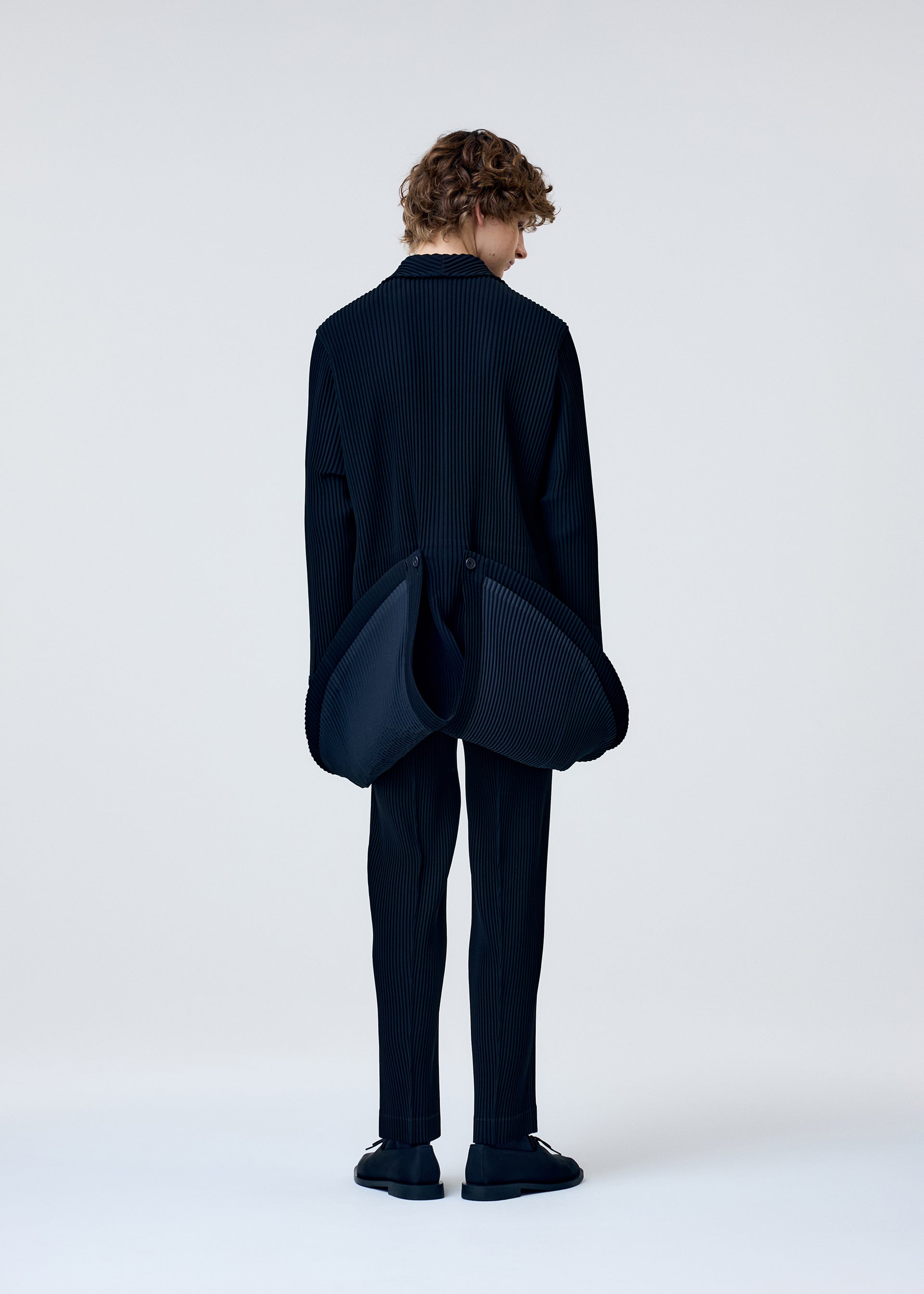 A model wears the HOMME PLISSÉ ISSEY MIYAKE TUXEDO PLEATS jacket.